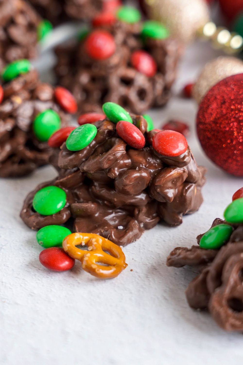 Crockpot Chocolate Pretzel Christmas Candy placed around a white table with a christmas ornament to side