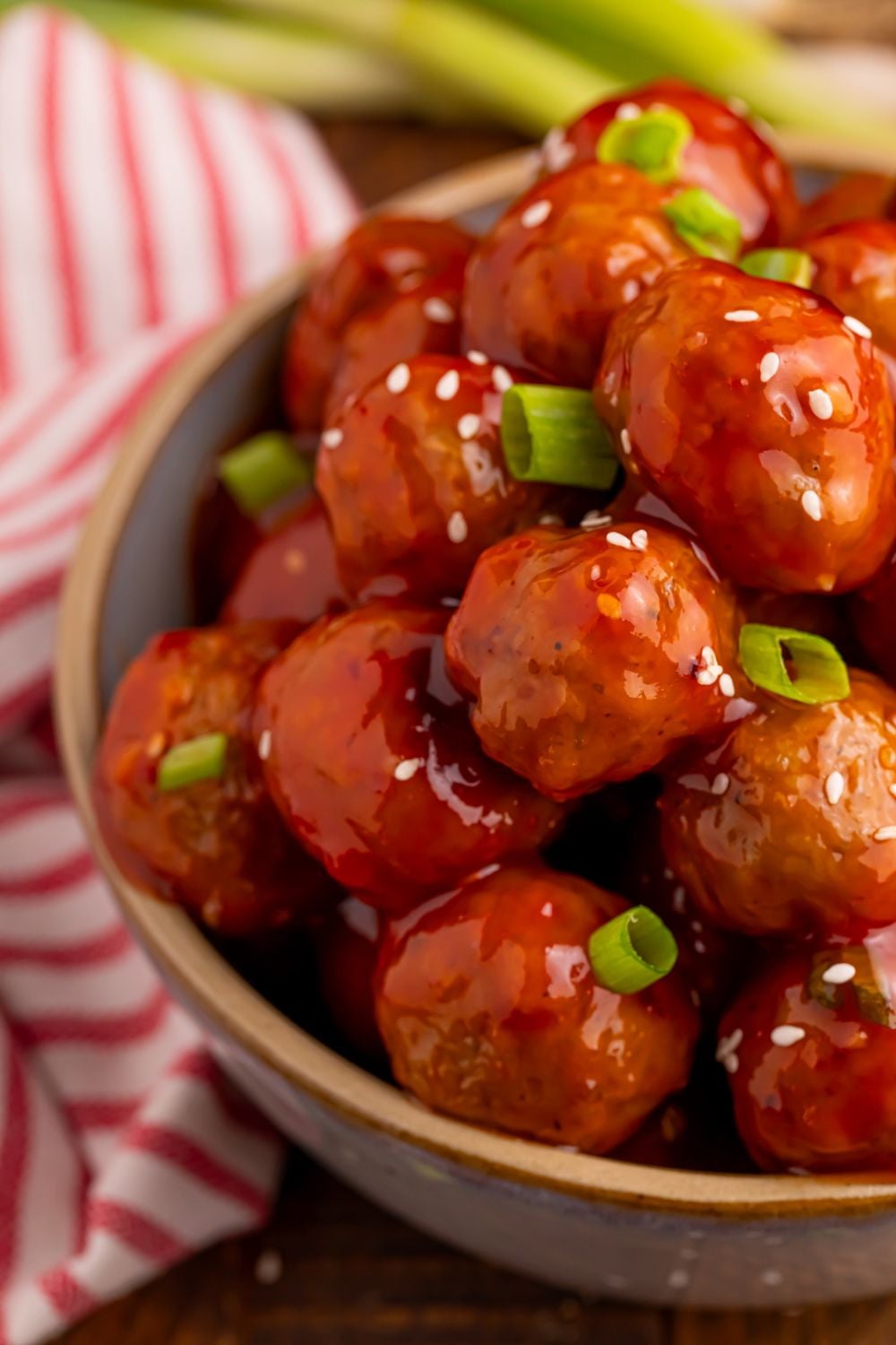 Crockpot Sweet Chili Meatballs in a ceramic bowl with a bundle of green onions behind bowl and red striped towel to side on table