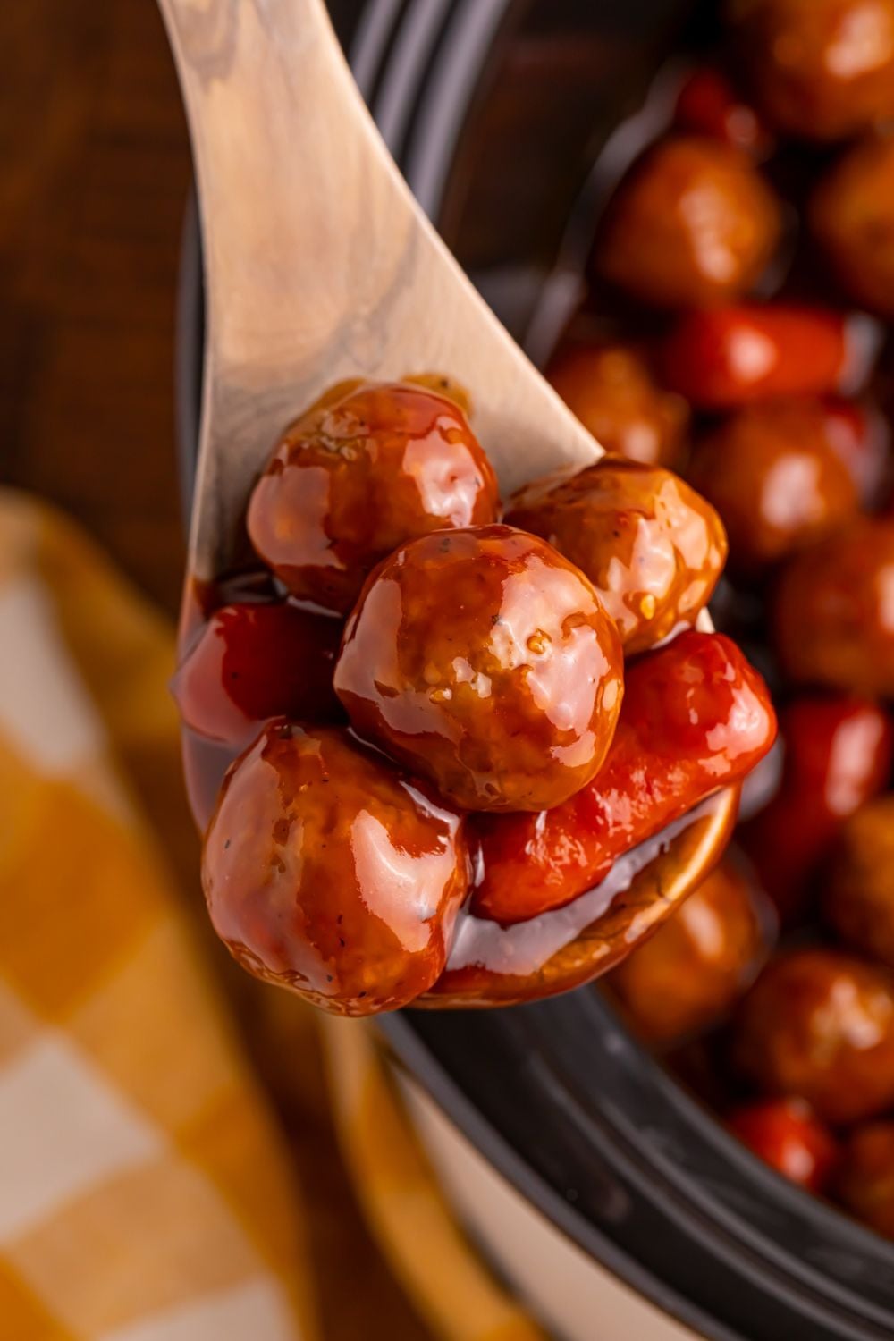 Crockpot Teriyaki BBQ Cocktail Meatballs & Lil Smokies on a wooden spoon above the crockpot on the wooden table 