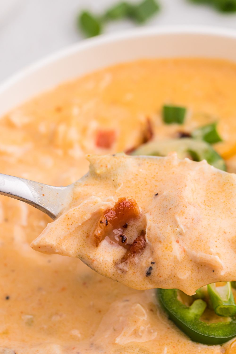 jalapeño popper crack chicken soup in a bowl with a spoon scooping up some of the soup
