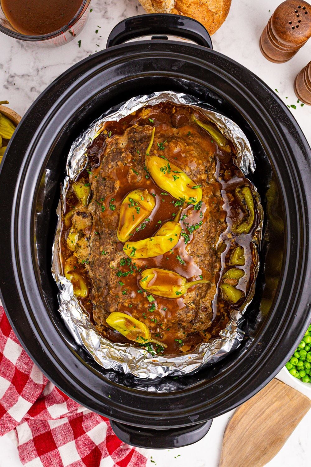 Crockpot Mississippi Meatloaf in a crockpot with peppers and gravy poured over the top of it on the table