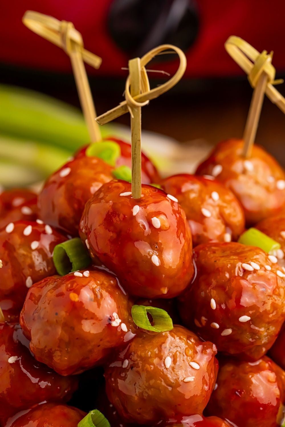 Crockpot Sweet Chili Meatballs with toothpicks in them on a platter on table with green onions and sesame seeds on top of the meatballs