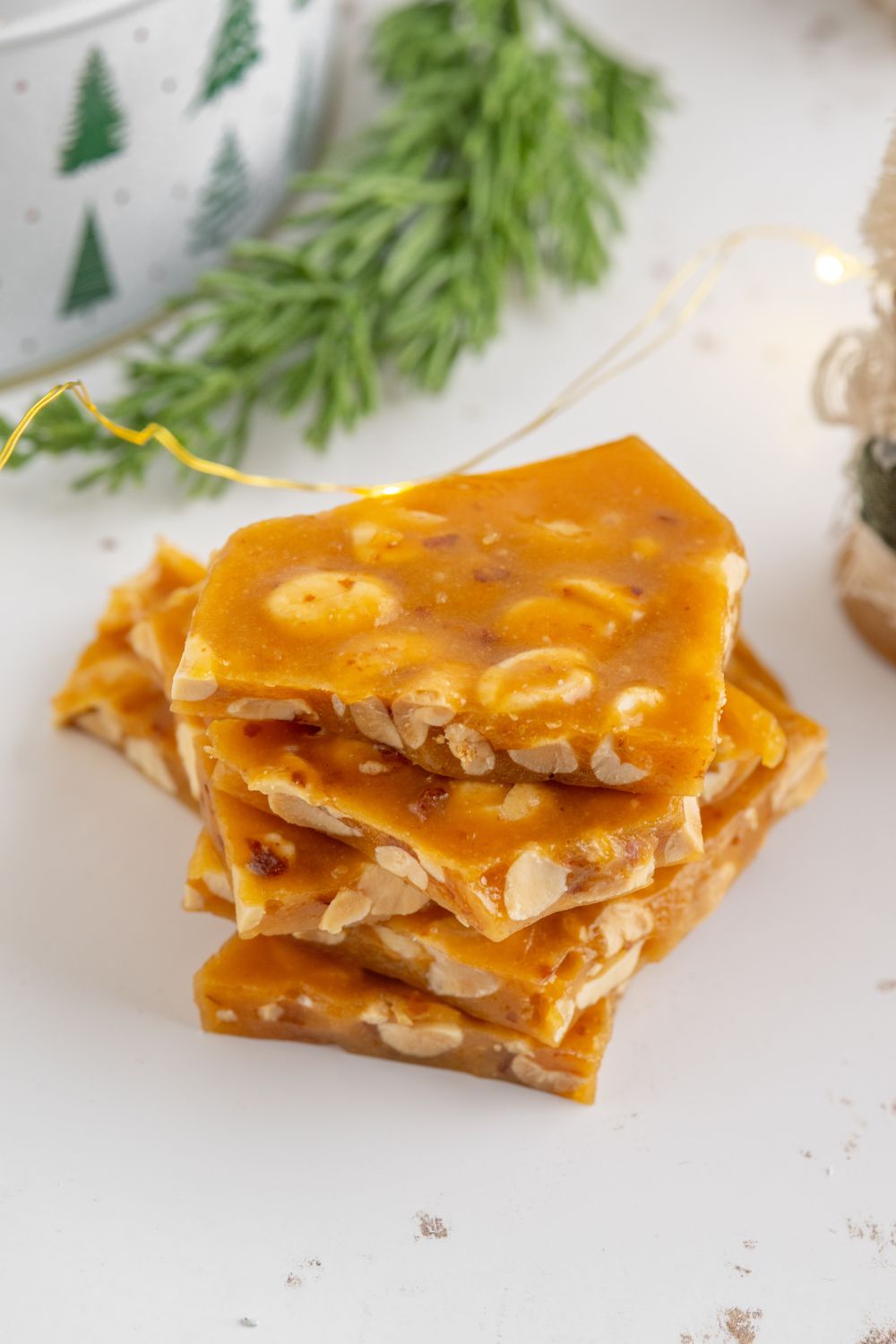 small batch peanut brittle broken into pieces on white table with Christmas decor behind table