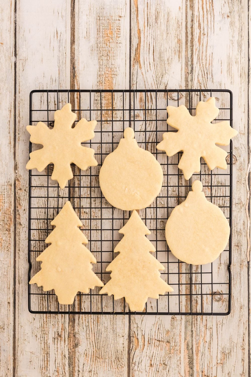 baked sugar cookies on a cooling rack on table that are shaped like Christmas decorations