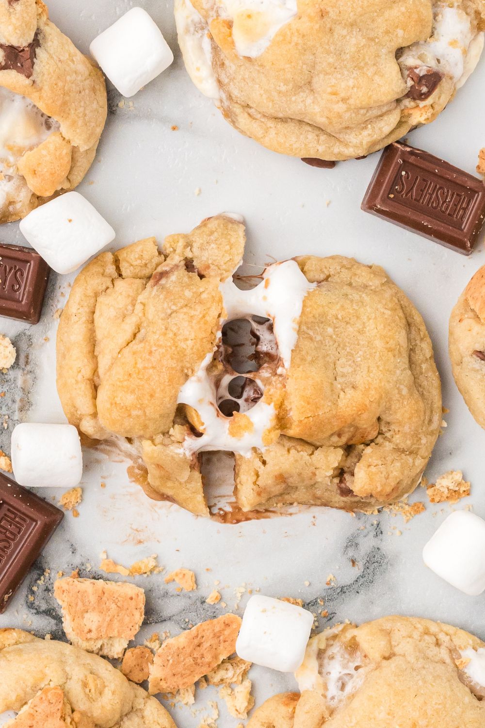 a smores cookie pulled apart on table to show chocolate and marshmallow pulling at both ends wit hmore cookies around them