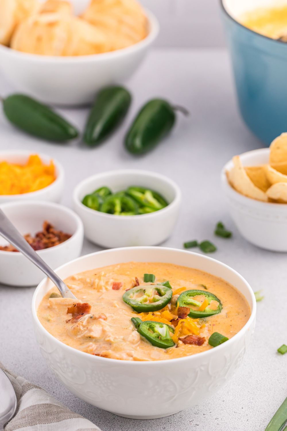 jalapeño popper crack chicken soup in a bowl with chips, peppers, and other ingredients around the table