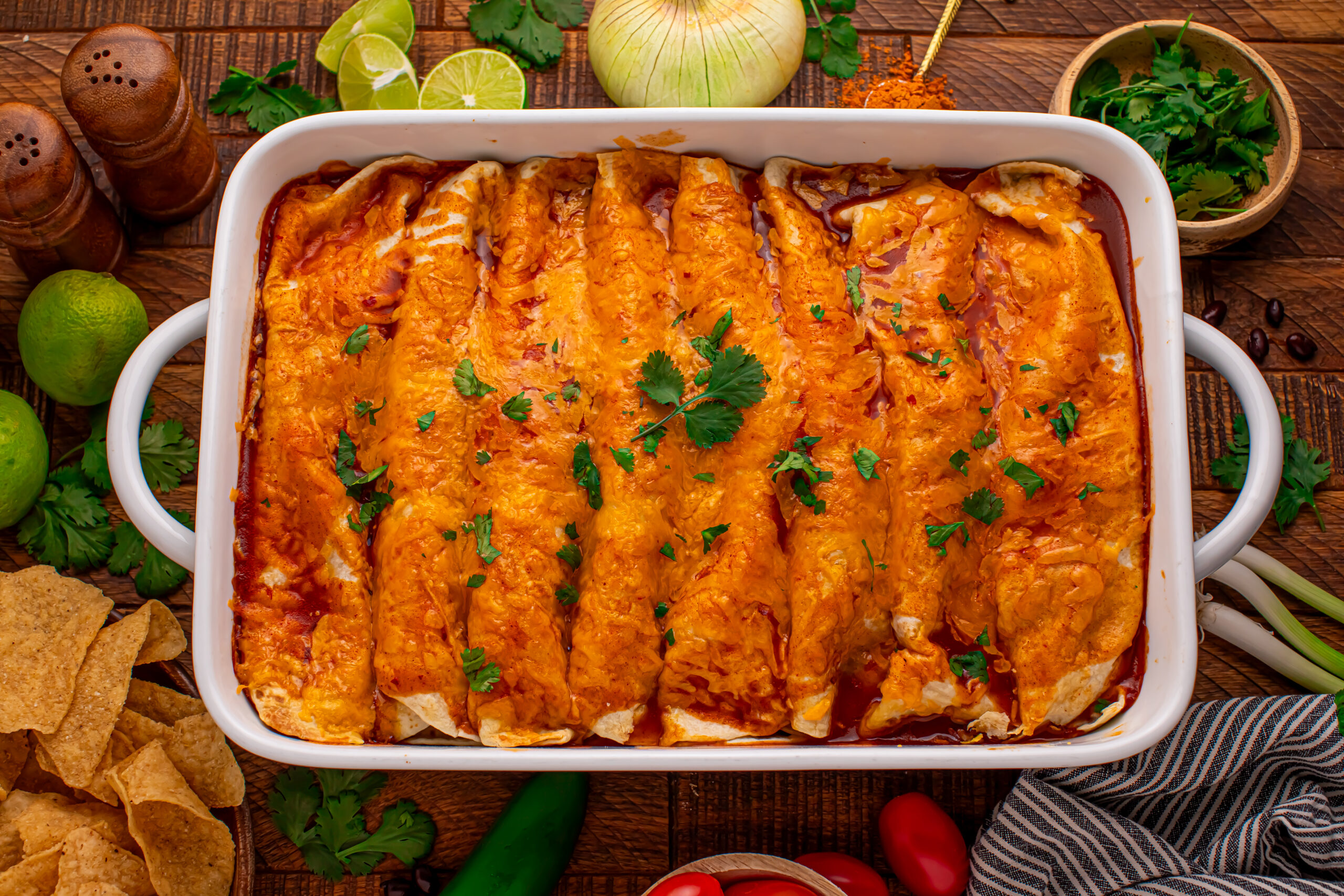 Steak Enchiladas in a white baking dish topped with sour cream and diced tomatoes