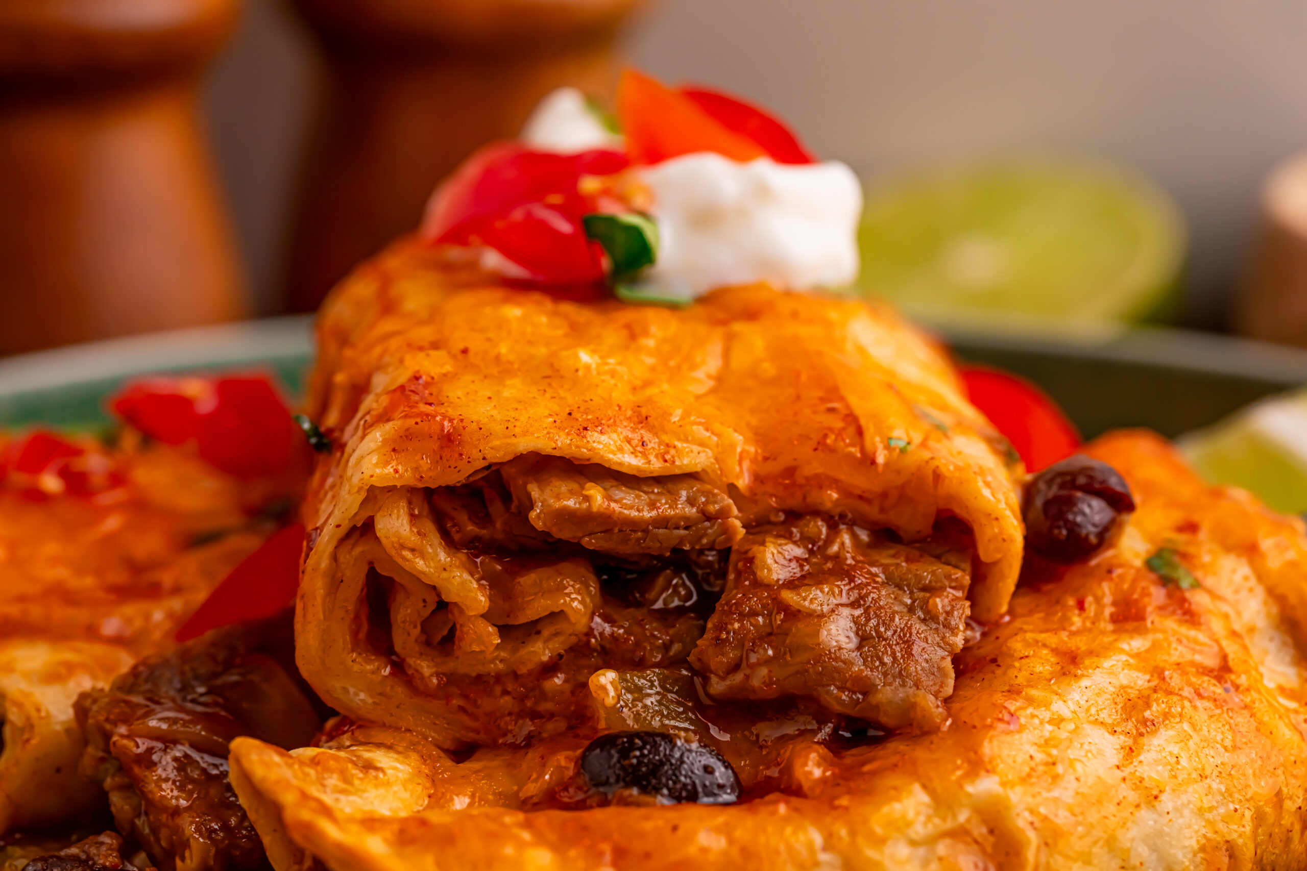 Steak Enchiladas on a green plate topped with sour cream and diced tomatoes