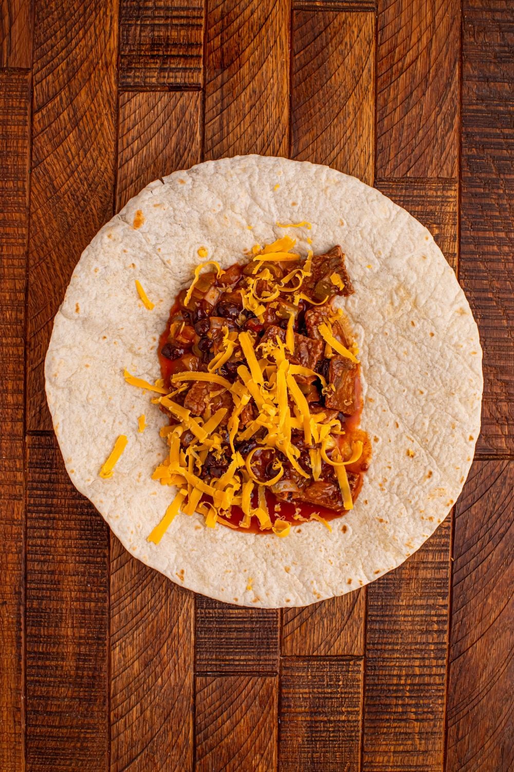 tortilla on wooden table full of a steak filling in center for making Steak Enchiladas