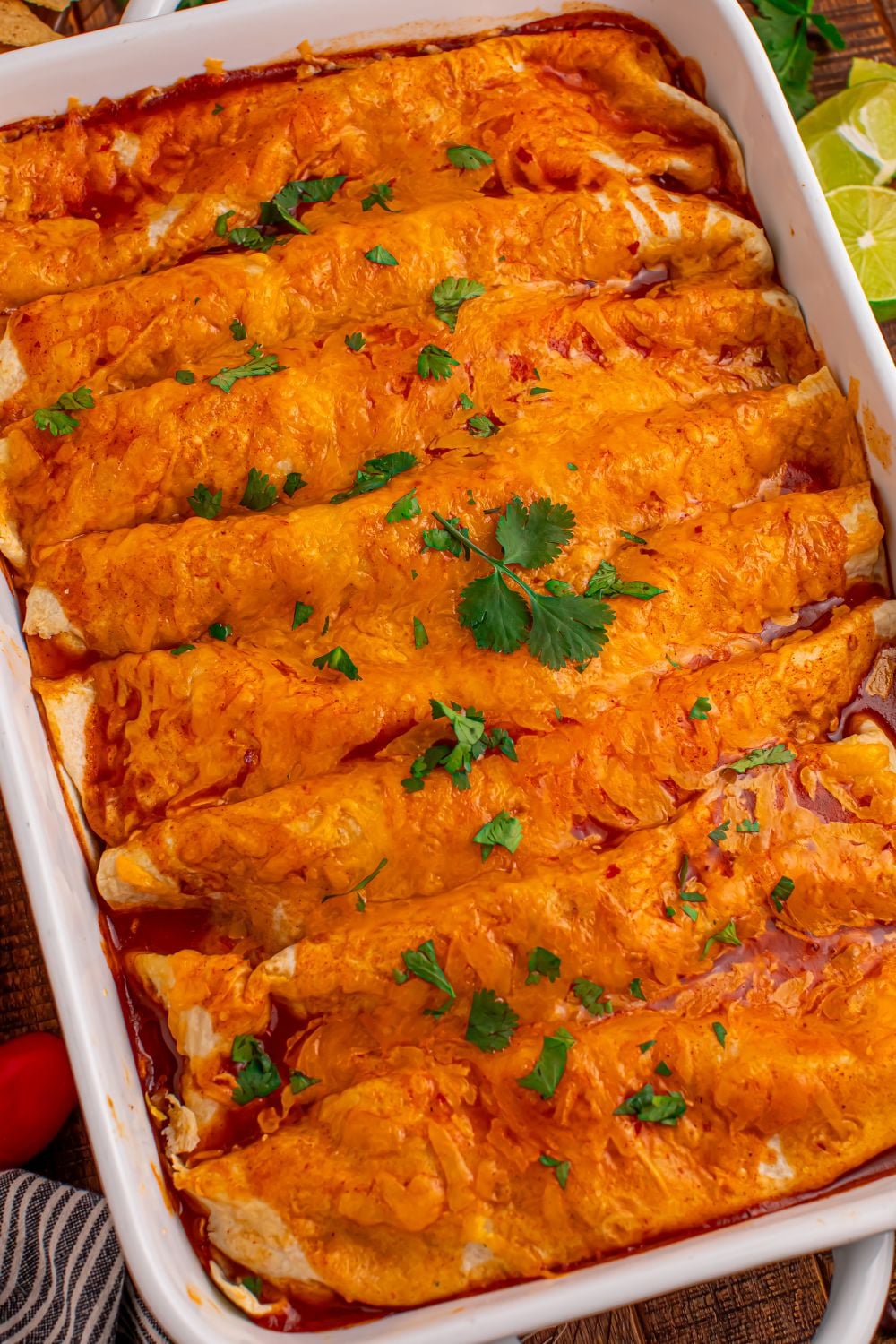 Steak Enchiladas in a white casserole dish on a wooden table slanted to side with some cilantro on top of the melted cheese