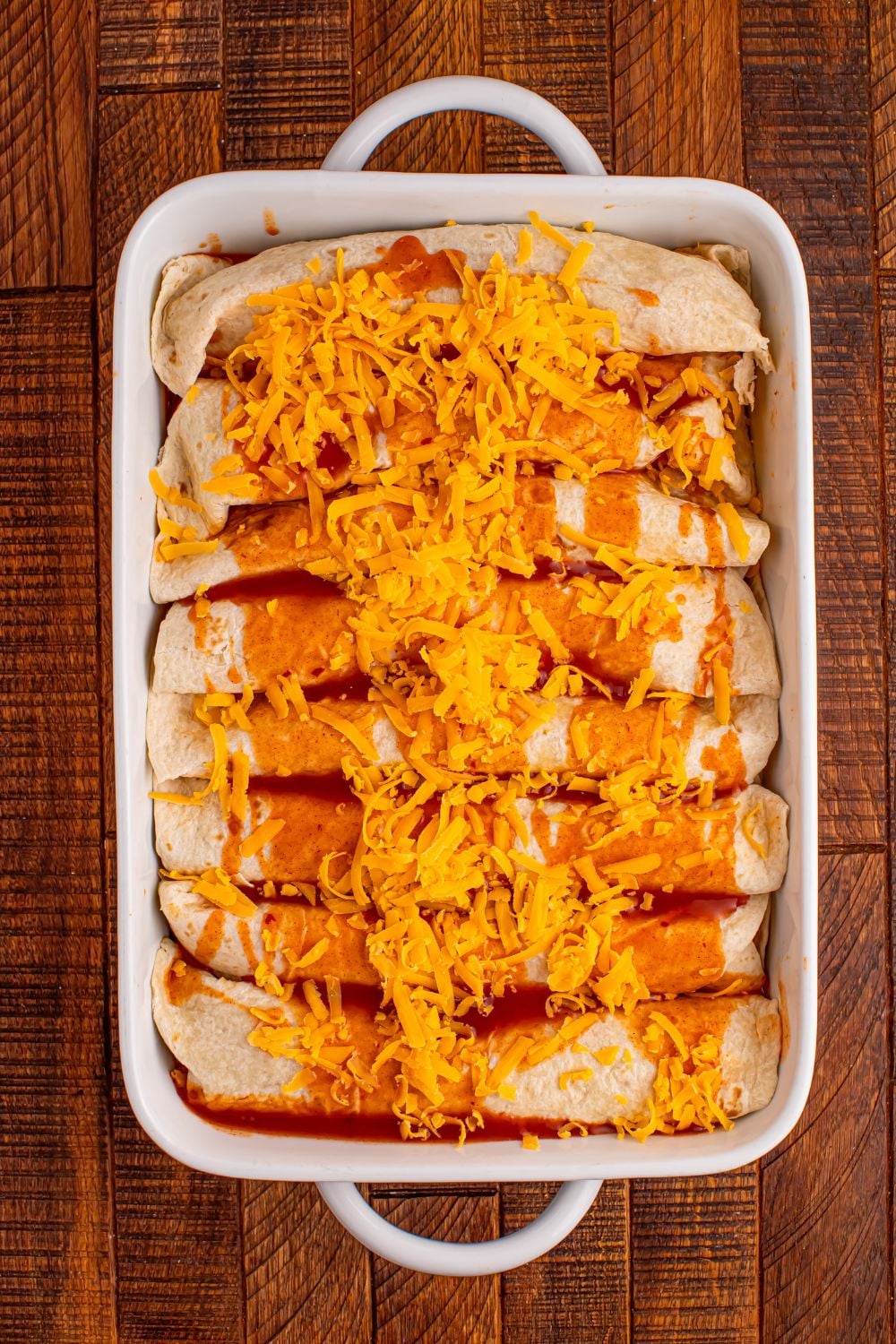 Steak Enchiladas being assembled and placed in a white casserole dish on the wooden table