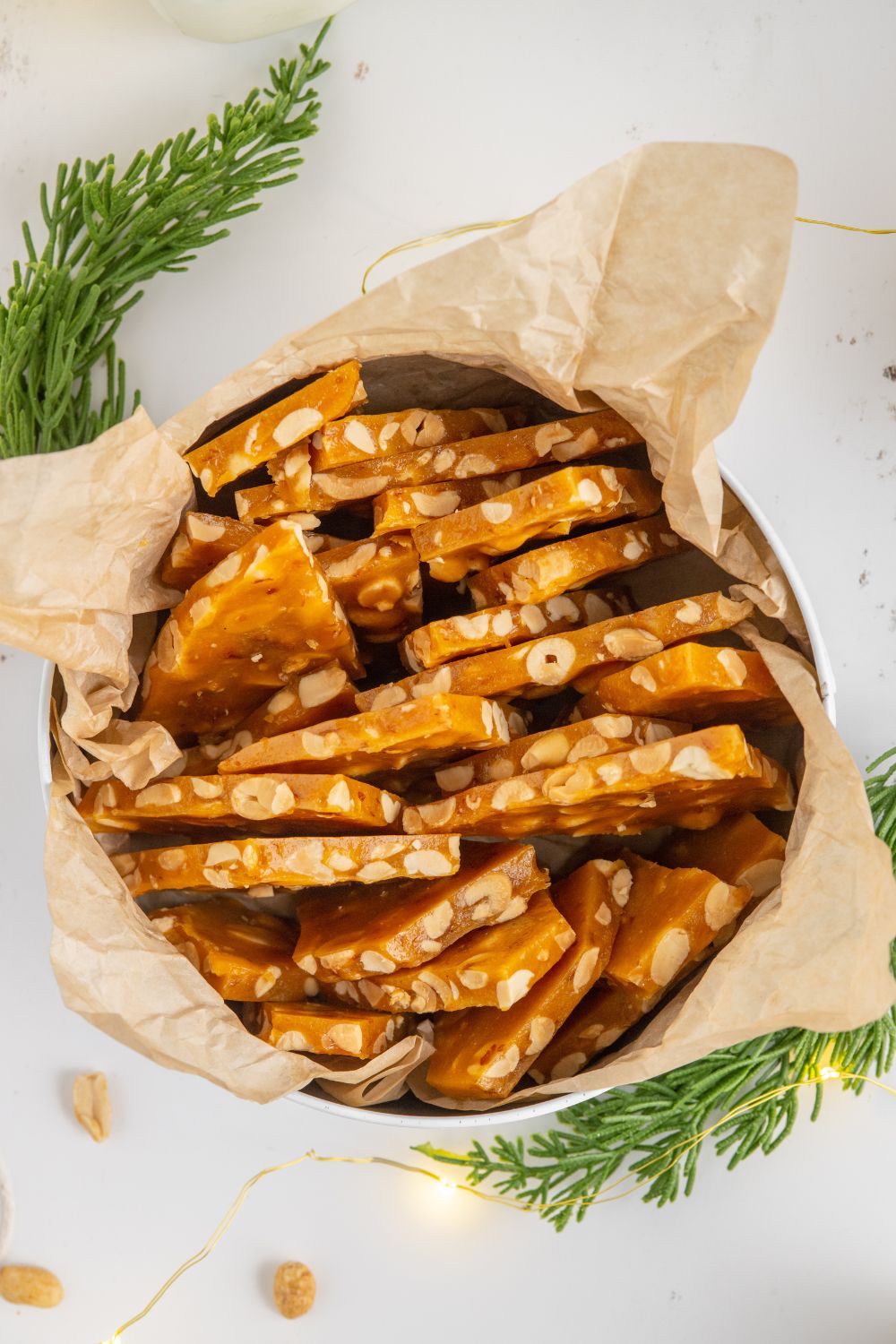 Homemade Peanut Brittle broken in a tin with christmas tree decor around the table