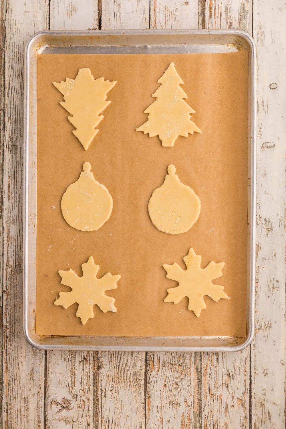 raw sugar cookie dough shaped like Christmas ornaments on a baking sheet