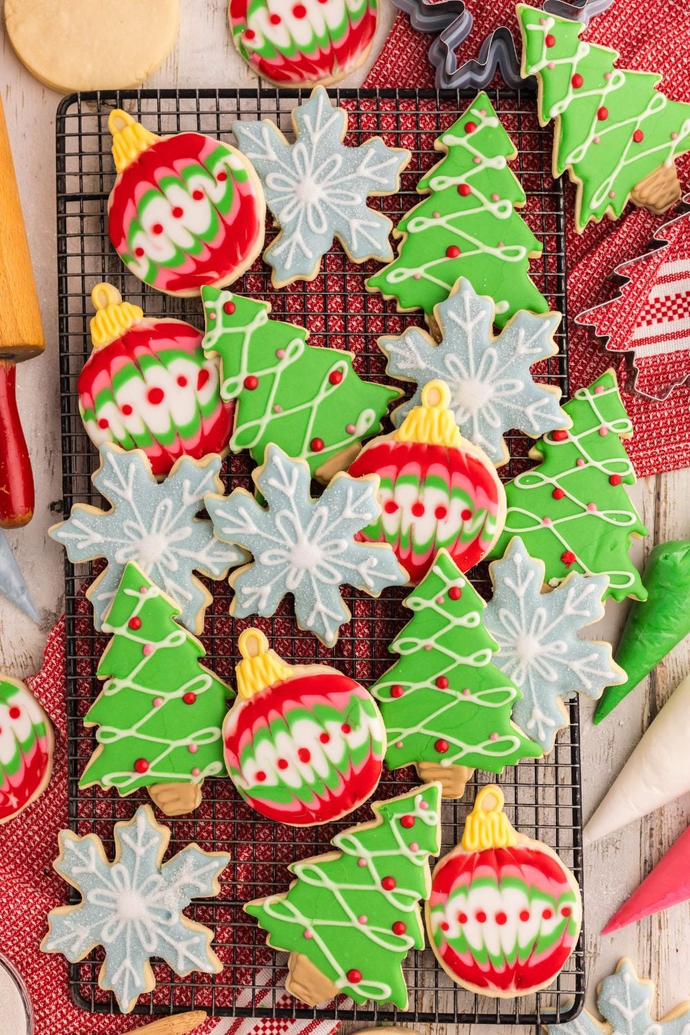 Decorated Sugar Cookies on a cooling rack all are decorated for Christmas with a red towel under the cooling rack