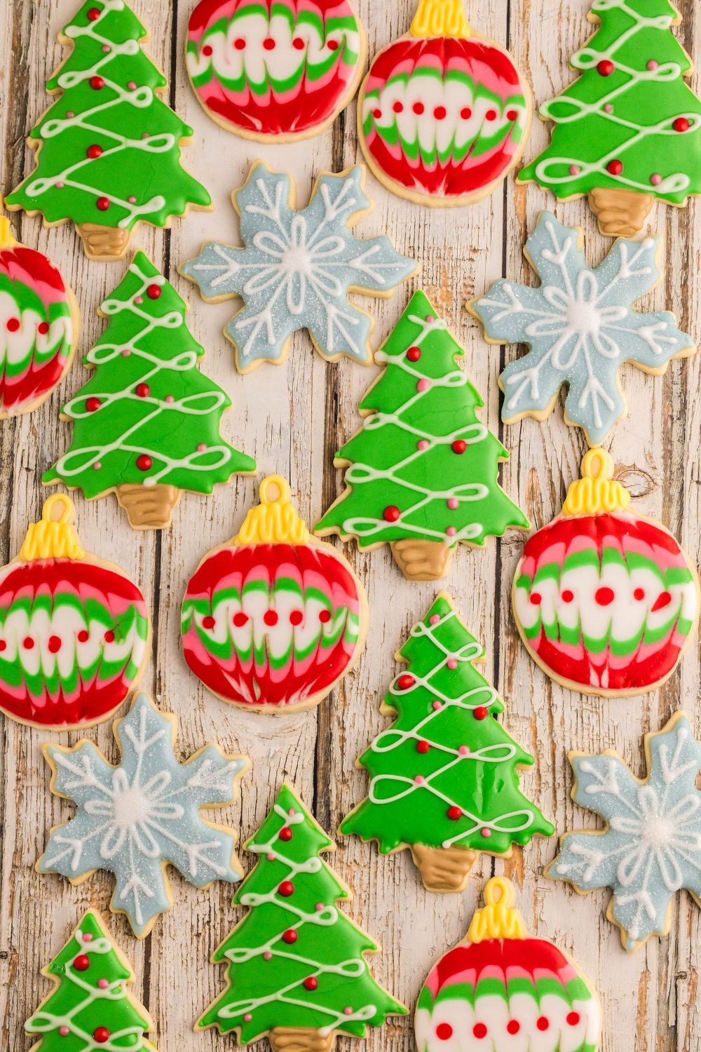 Christmas themed Decorated Sugar Cookies spread out all around a wooden table to show the colors and shapes of each cookie