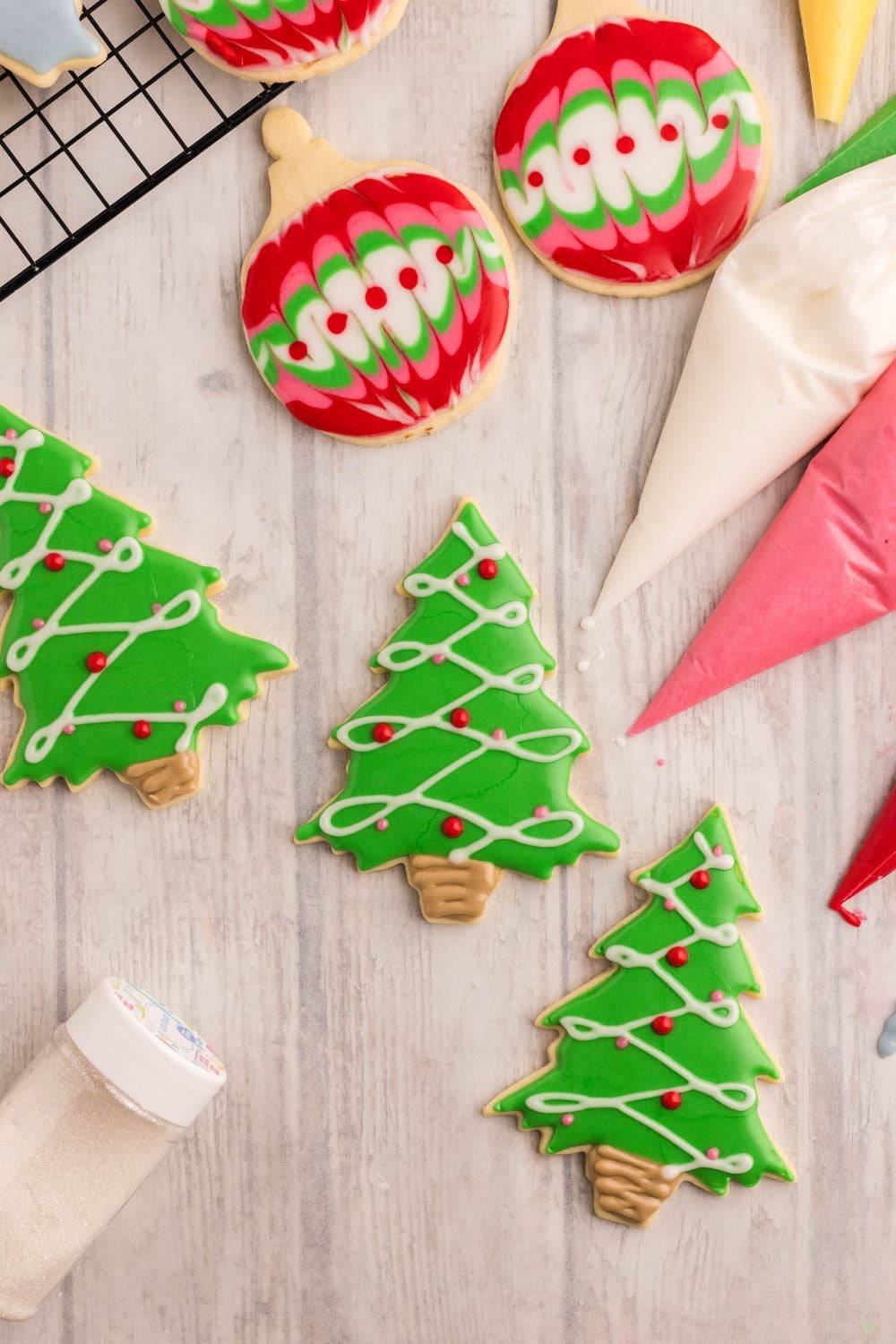 piping bags with royal icing to side and Christmas tree shaped cookies in front and a cooling rack to the back of photo