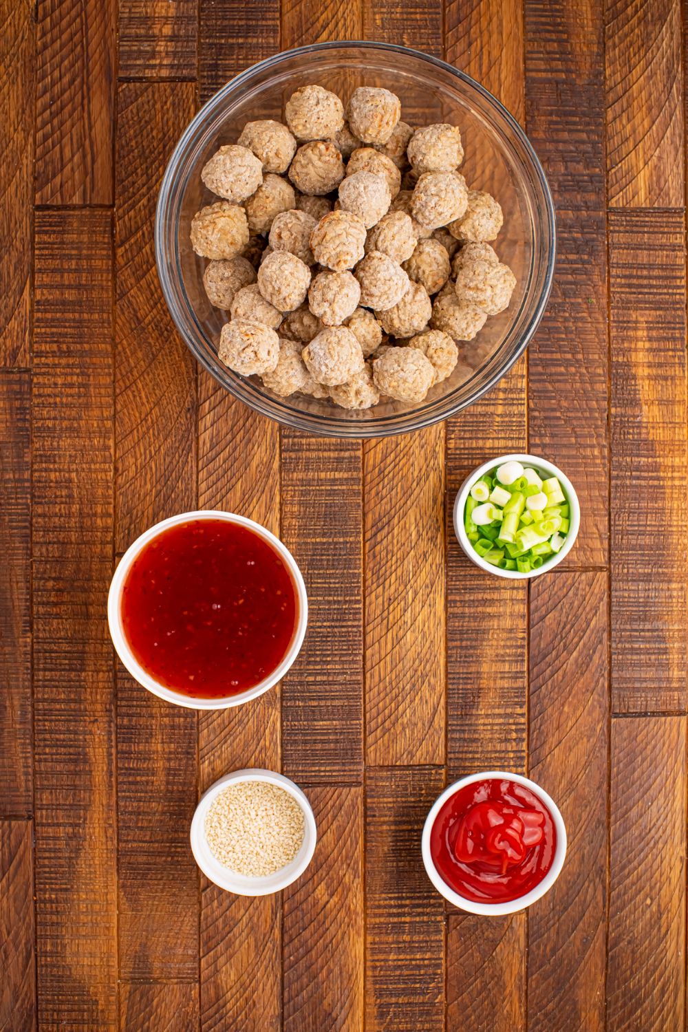 a glass bowl of frozen meatballs on wooden table with sweet chili sauce, green onions all in single serve bowls on the table