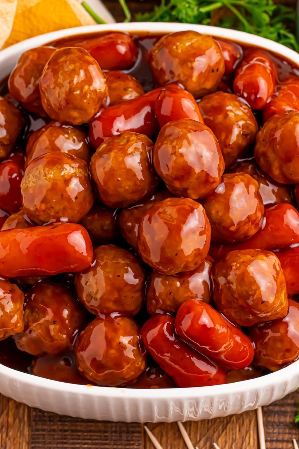 a white bowl full of Crockpot Teriyaki BBQ Cocktail Meatballs & Lil Smokies with some parsley behind it on the table 