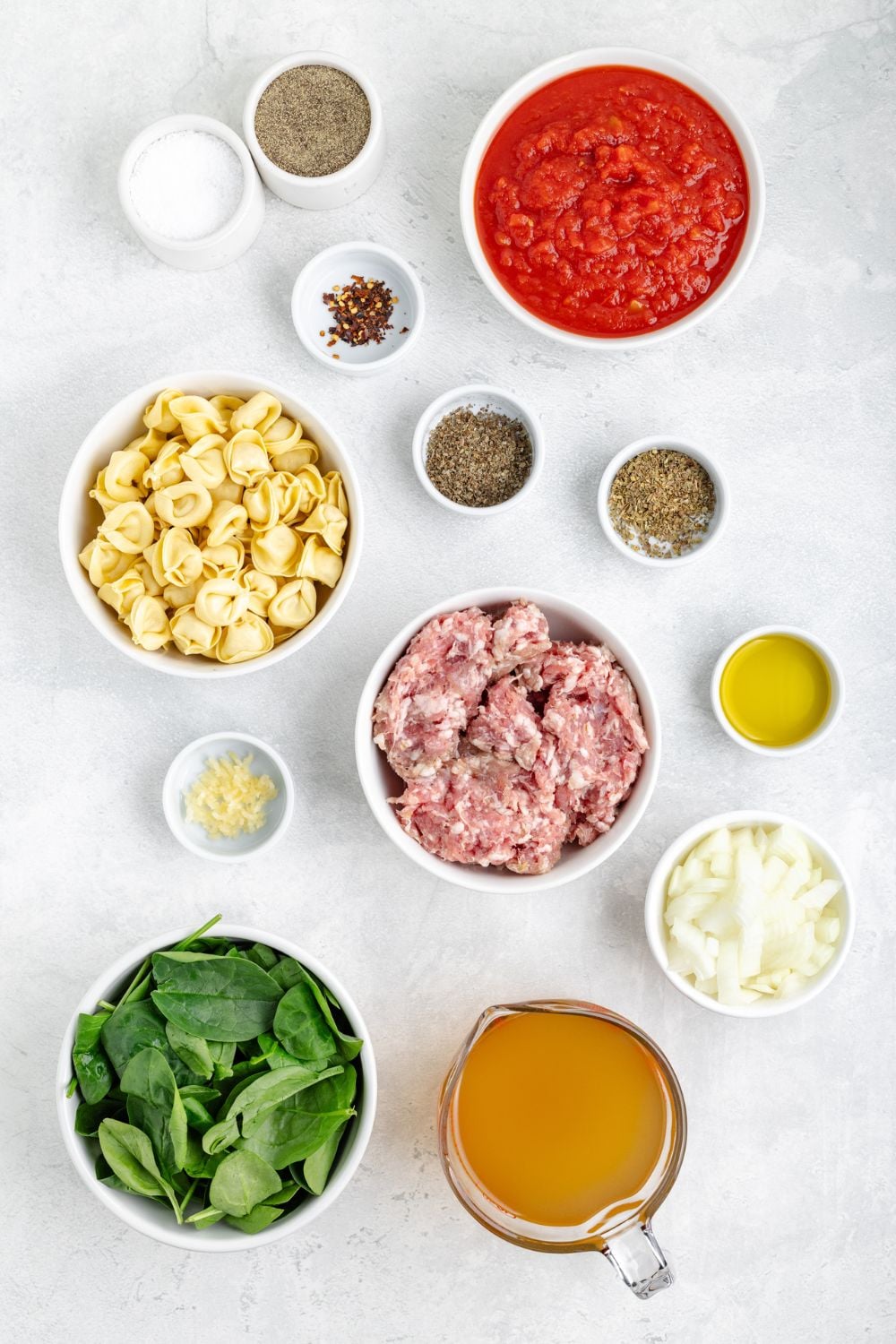 all the ingredients for Sausage Tortellini Soup in single serve bowls on a white table