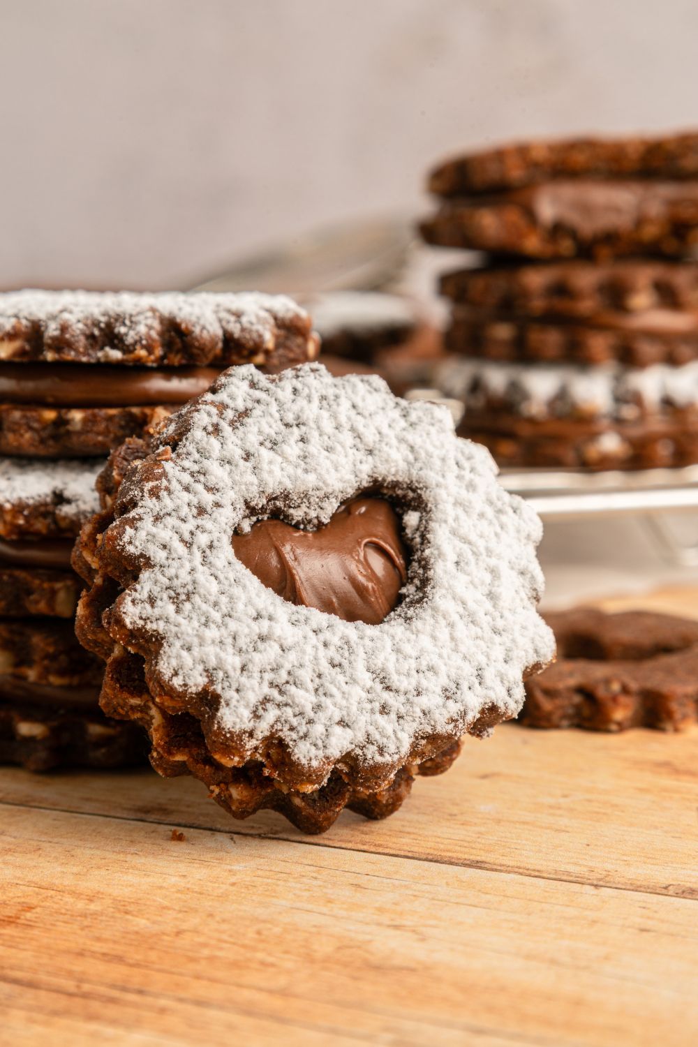 Chocolate Linzer Cookies spread around the table and one that is tilted to side to see the heart center 