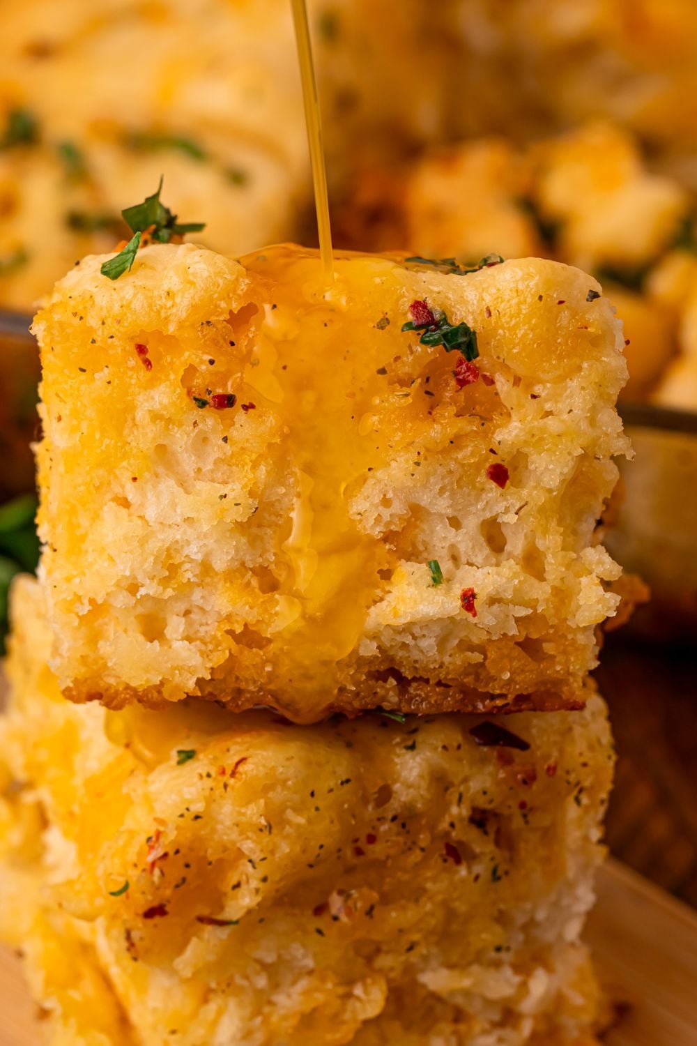 stacked Cowboy Butter Swim Biscuits on table with butter pouring over the top of them with some parsley in the background
