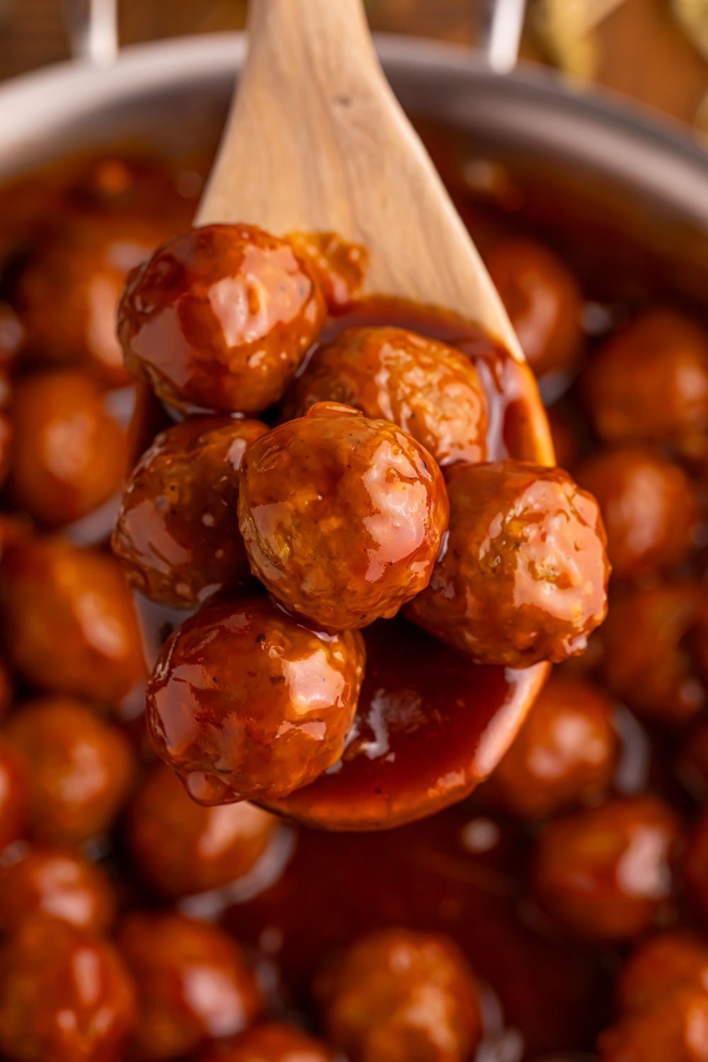 Peach BBQ Meatballs on a wooden spoon above a skillet on the table