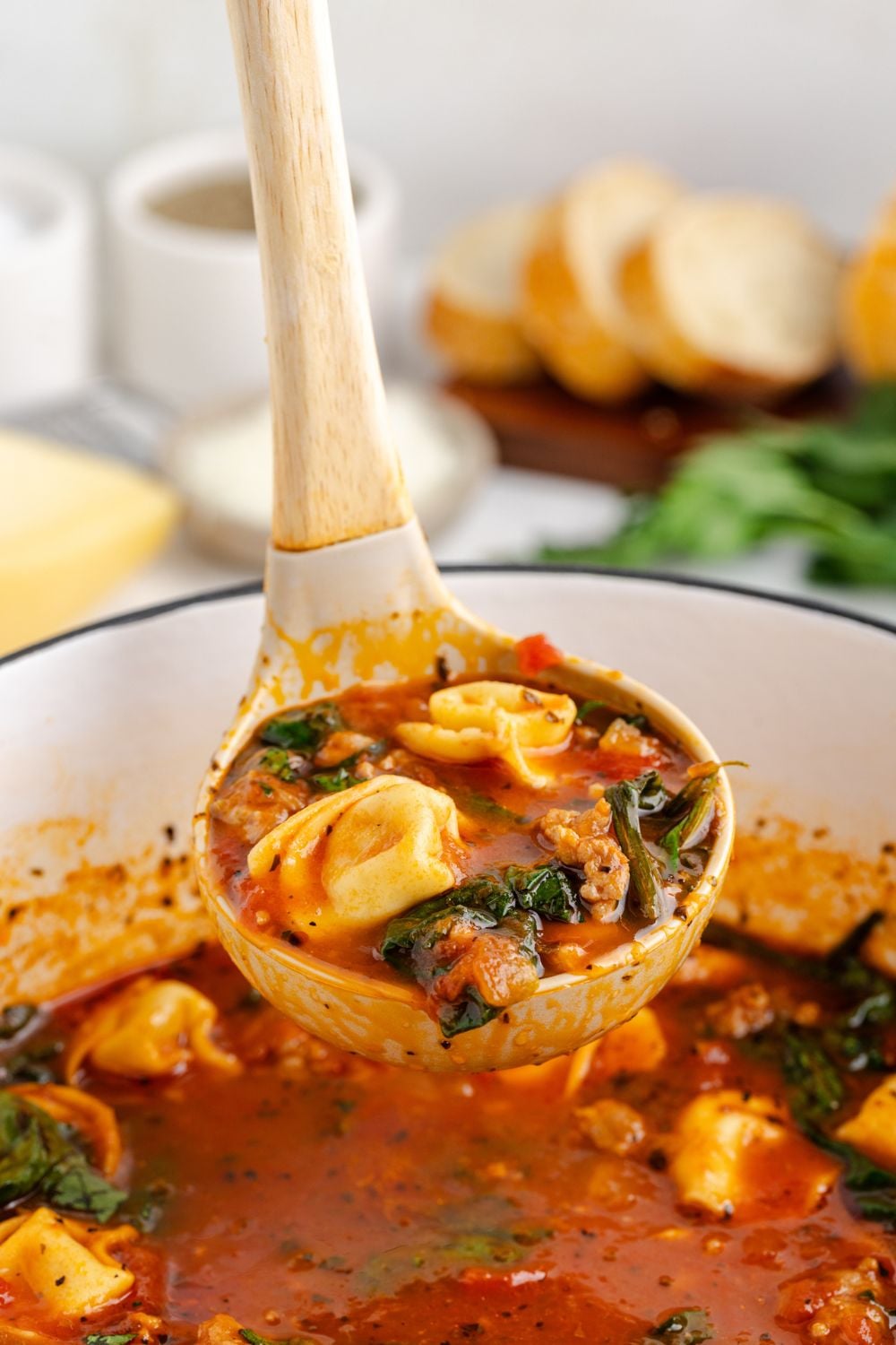 Sausage Tortellini Soup being lifted out of a white pot on table with a ladle full of the soup
