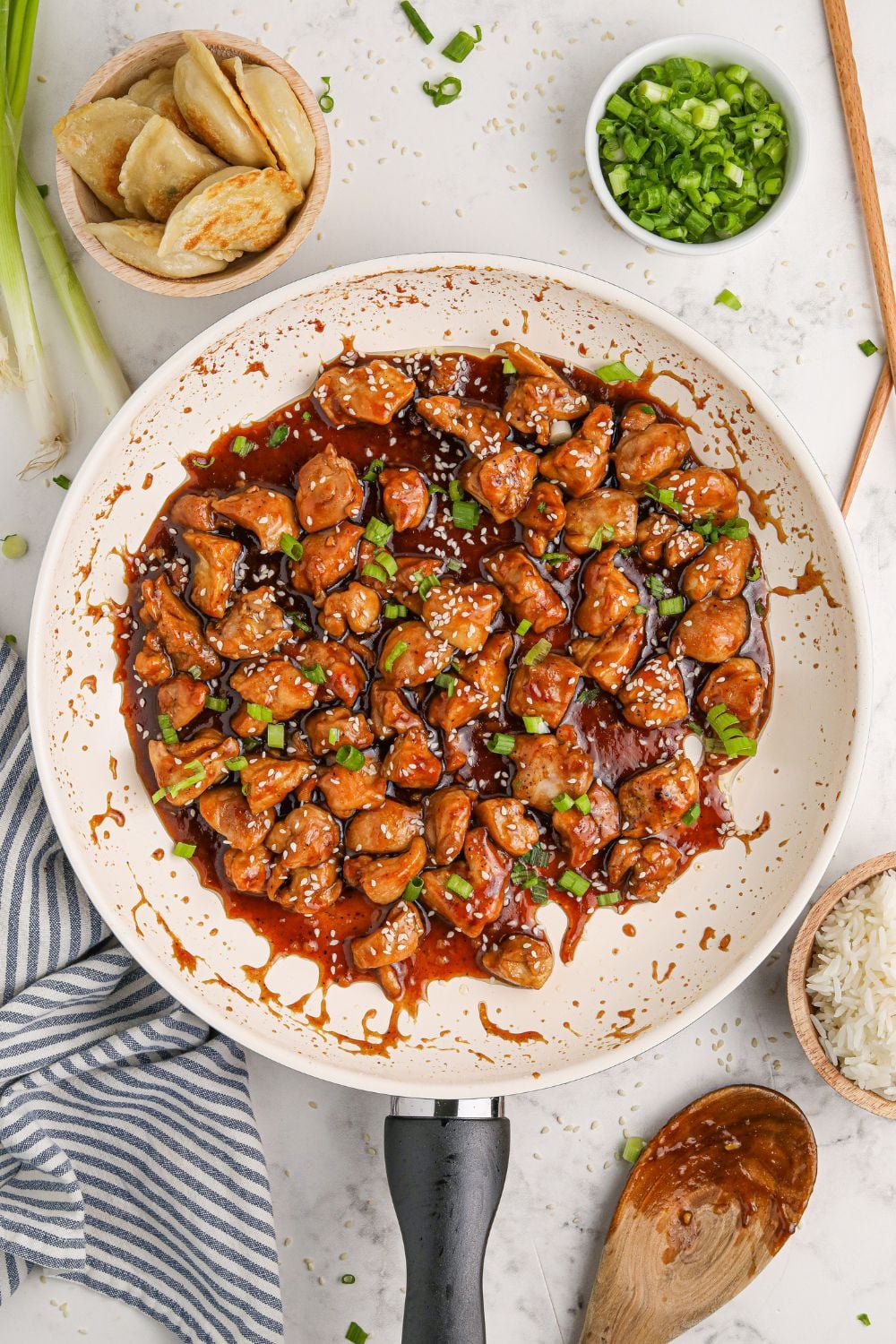 a skillet on the table with diced Bourbon Chicken Skillet to the side and green onions to the side on the plate