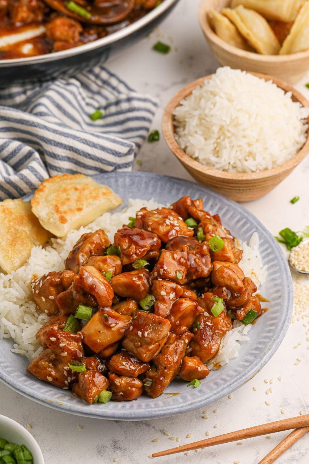 Bourbon Chicken on a plate with rice to side and bread, with a bowl of rice and more chicken spread out on the table