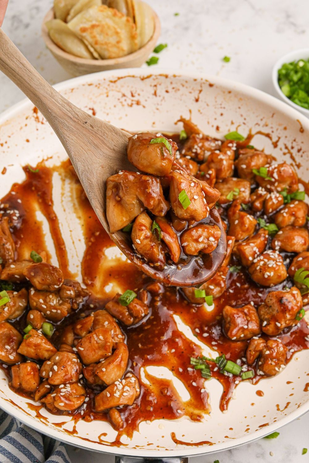 skillet with Bourbon Chicken in it with sauce and a spoon scooping up the chicken