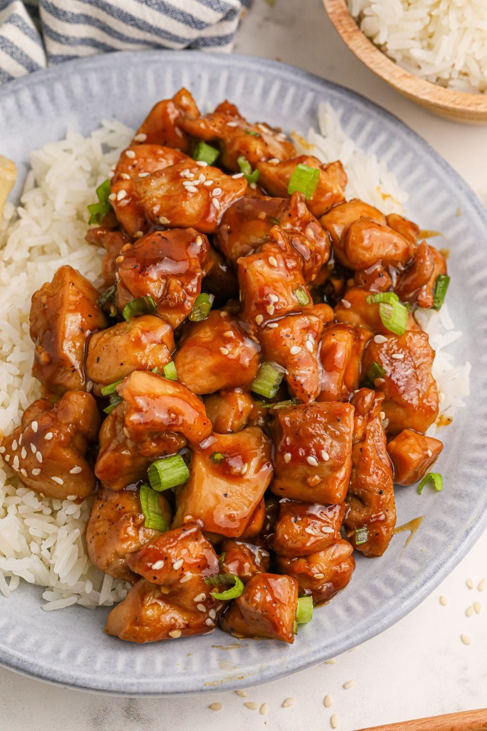 looking down on table with a plate full of diced skillet bourbon chicken and a bed of rice to the side and a red and grey striped towel to side
