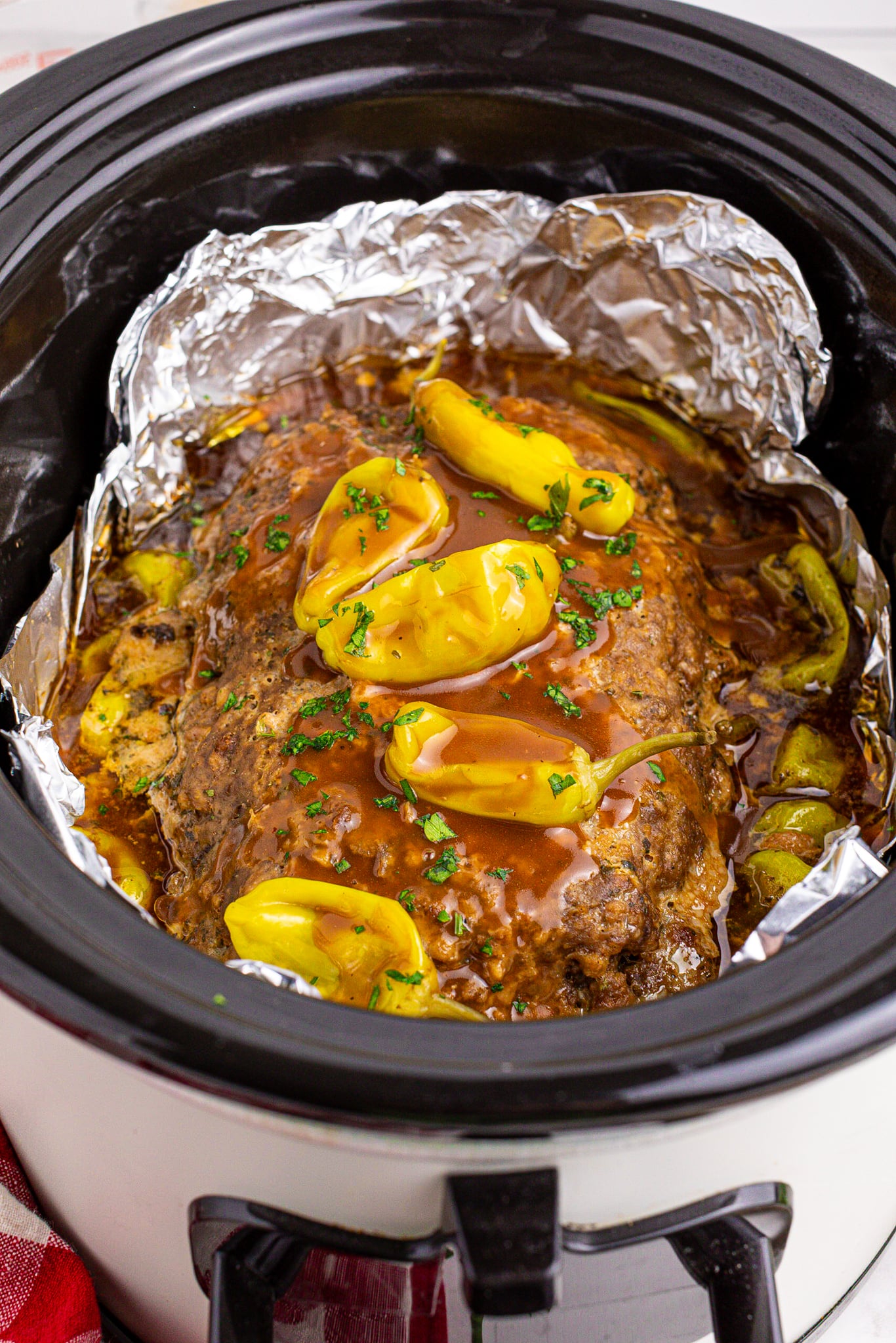 Crockpot Mississippi Meatloaf in a black slow cooker lined with foil topped with gravy and peppers