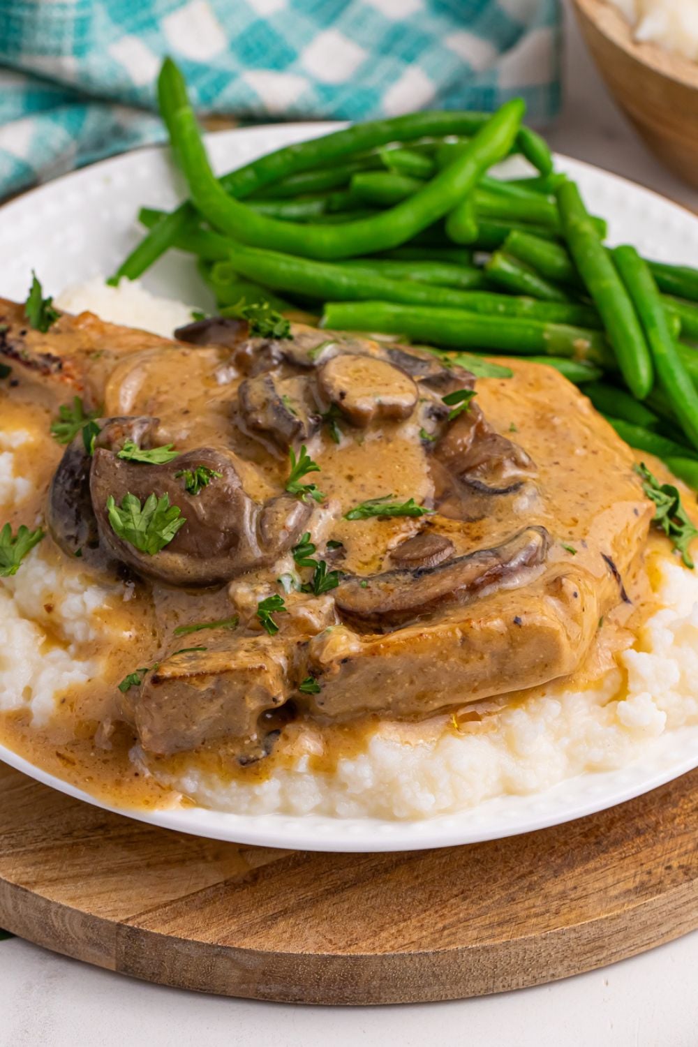 a plate with mashed potatoes and pork chop on top with fresh green beans and a towel behind the plate 