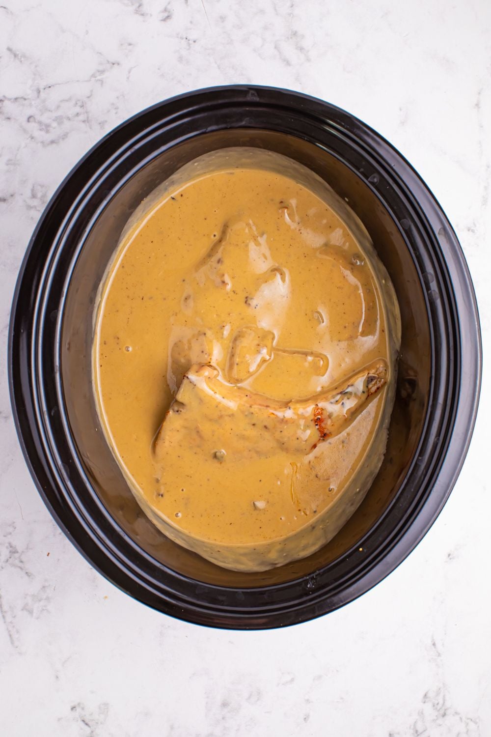 crockpot on marble counter table with pork chop and gravy mixture 