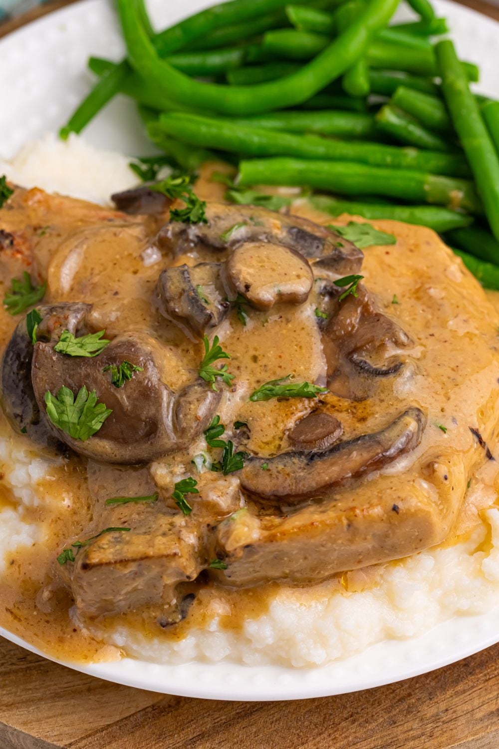close up look of smothered pork chop with mushrooms on plate with green beans 