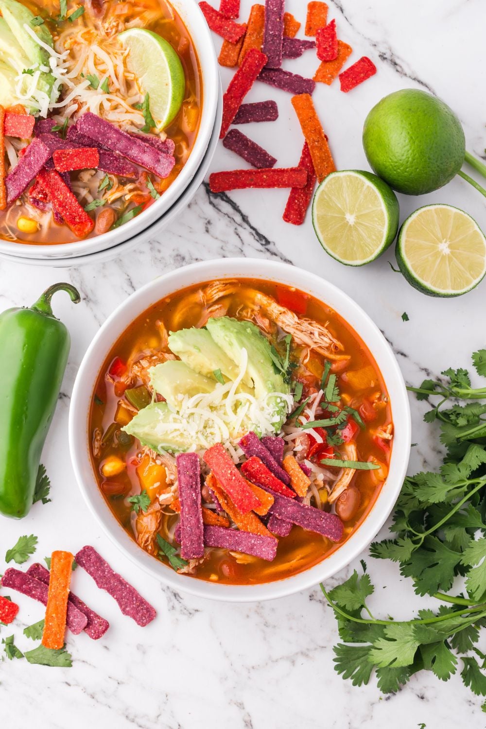 Southwestern Chicken Soup in bowls on a marble table with cilantro, peppers, and sliced limes on the table