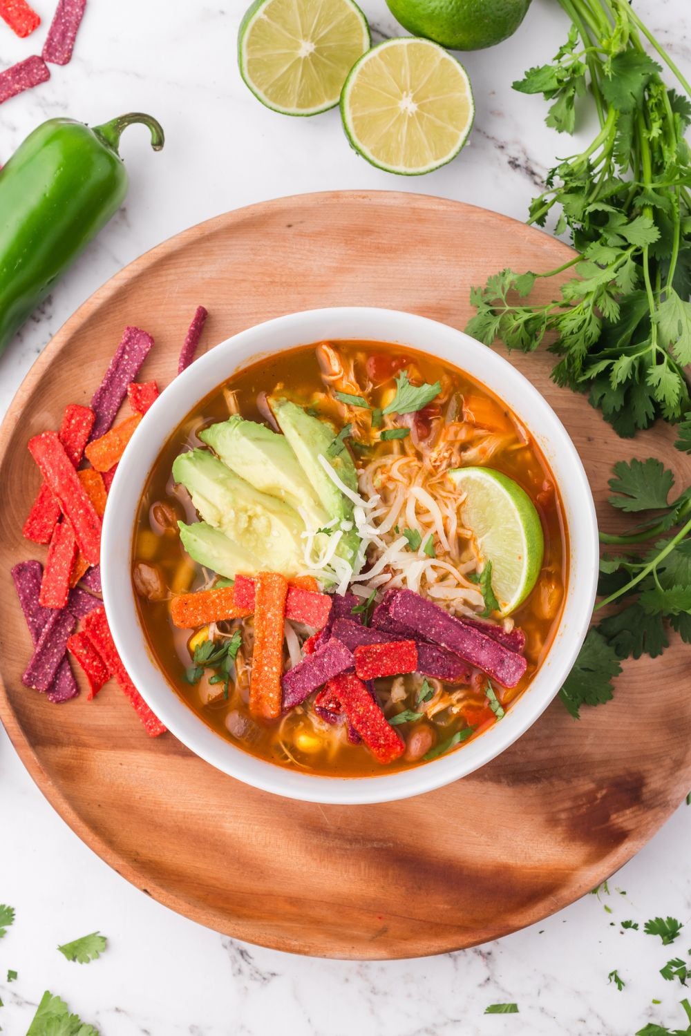 Southwestern Chicken Soup in a white bowl sitting on a round wooden board, with all the topping ideas spread around on the table