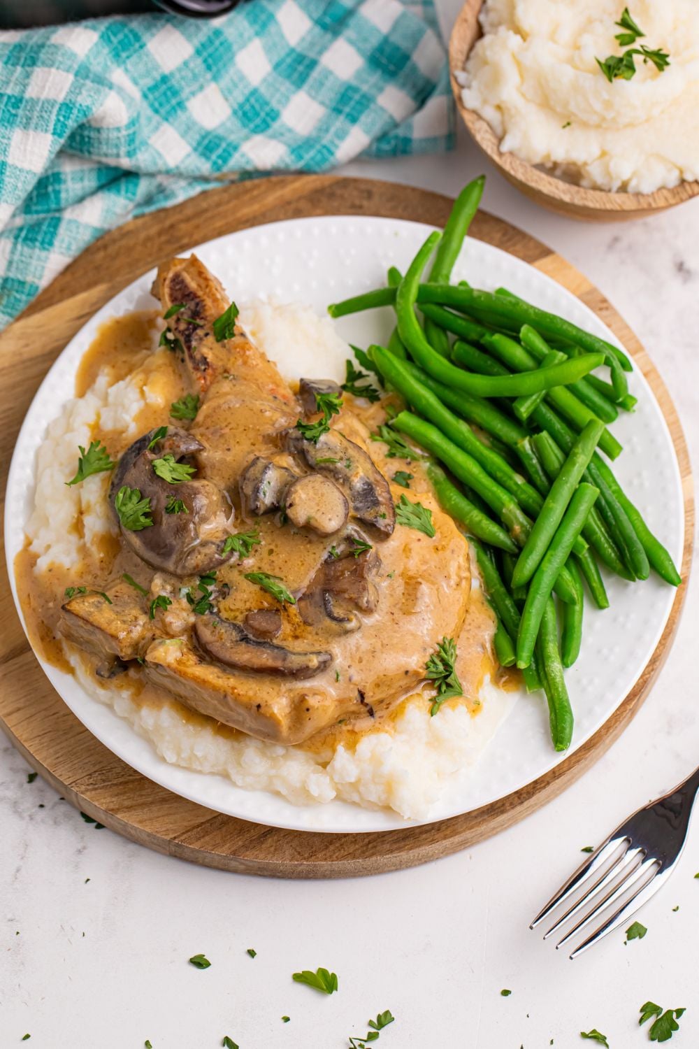 plate with pork chop with gravy and mashed potatoes and fresh green beans on a plate and a bowl of potatoes to side 