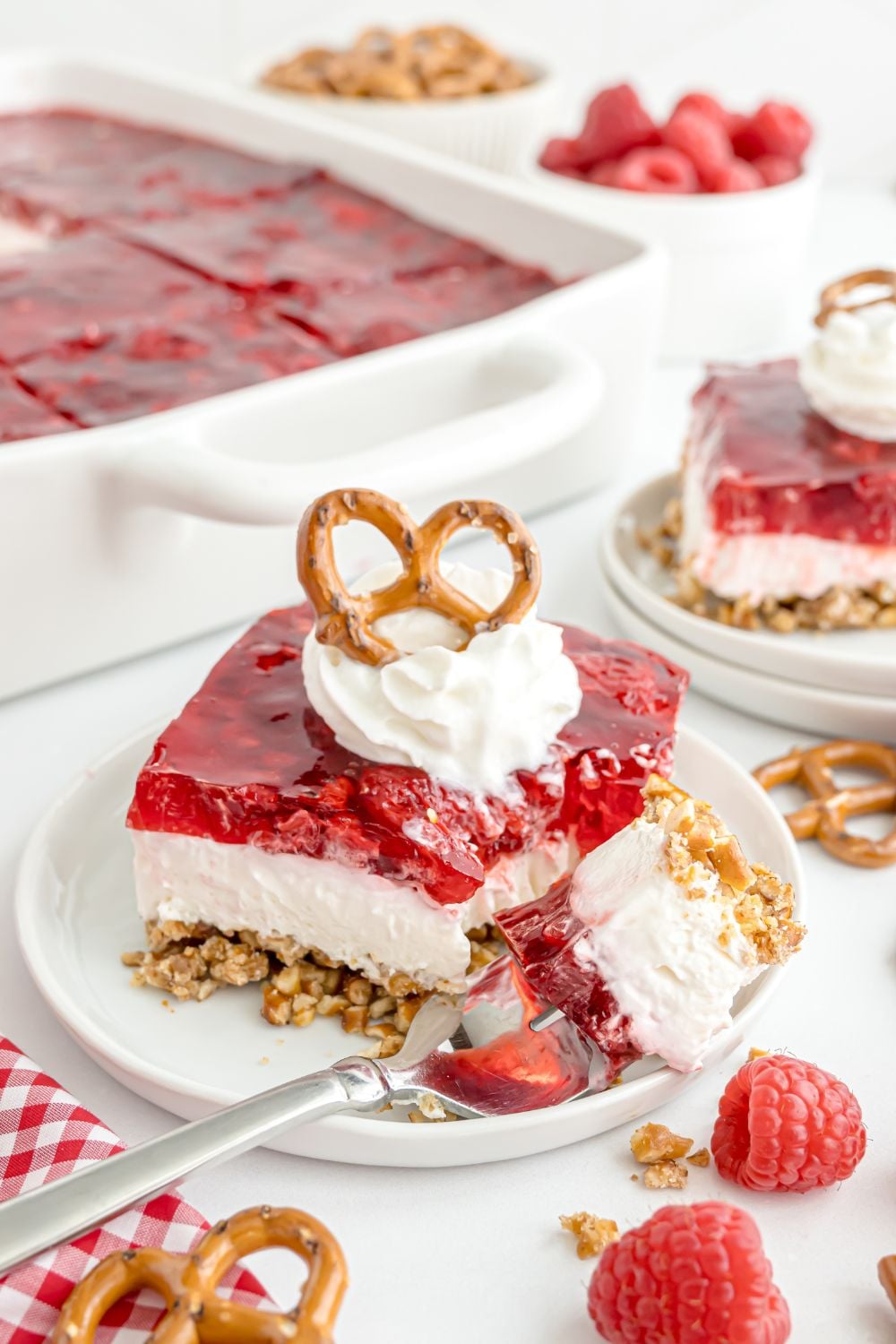 Raspberry Pretzel Salad in a pan and then in front plates with slices of raspberry pretzel salad spread around the table