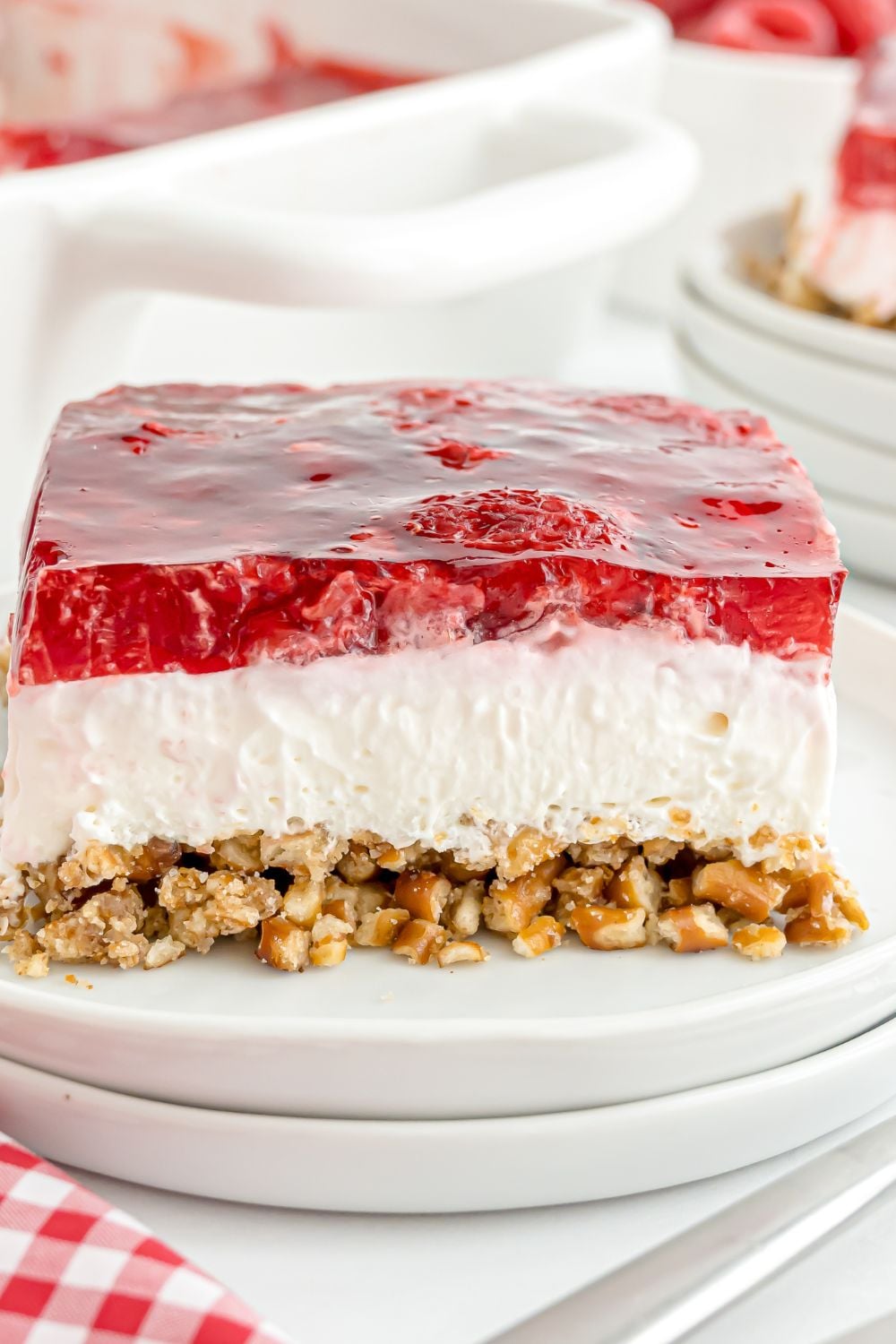 two white plates stacked on top of one another with a slice of Raspberry Pretzel Salad on it showing all the layers of the dessert