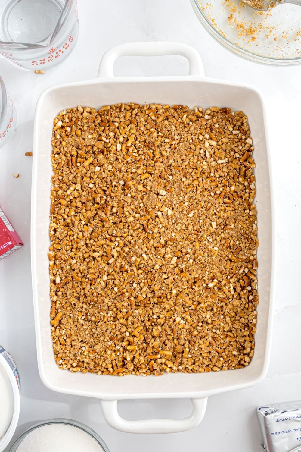 crushed pretzel mixture in a casserole dish sitting on table to make Raspberry Jello salad with pretzels