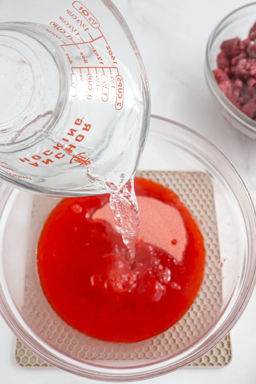 raspberry jello in a bowl with water pouring over the top of the jello