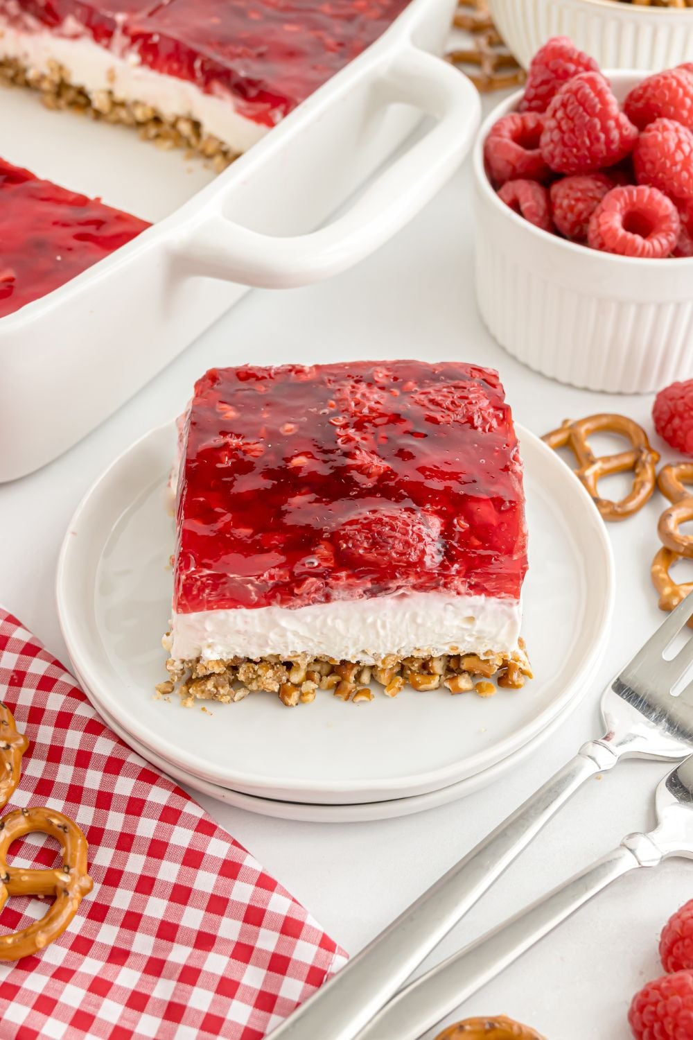 Raspberry Pretzel Salad on a plate with more pretzels and berries scattered around the table