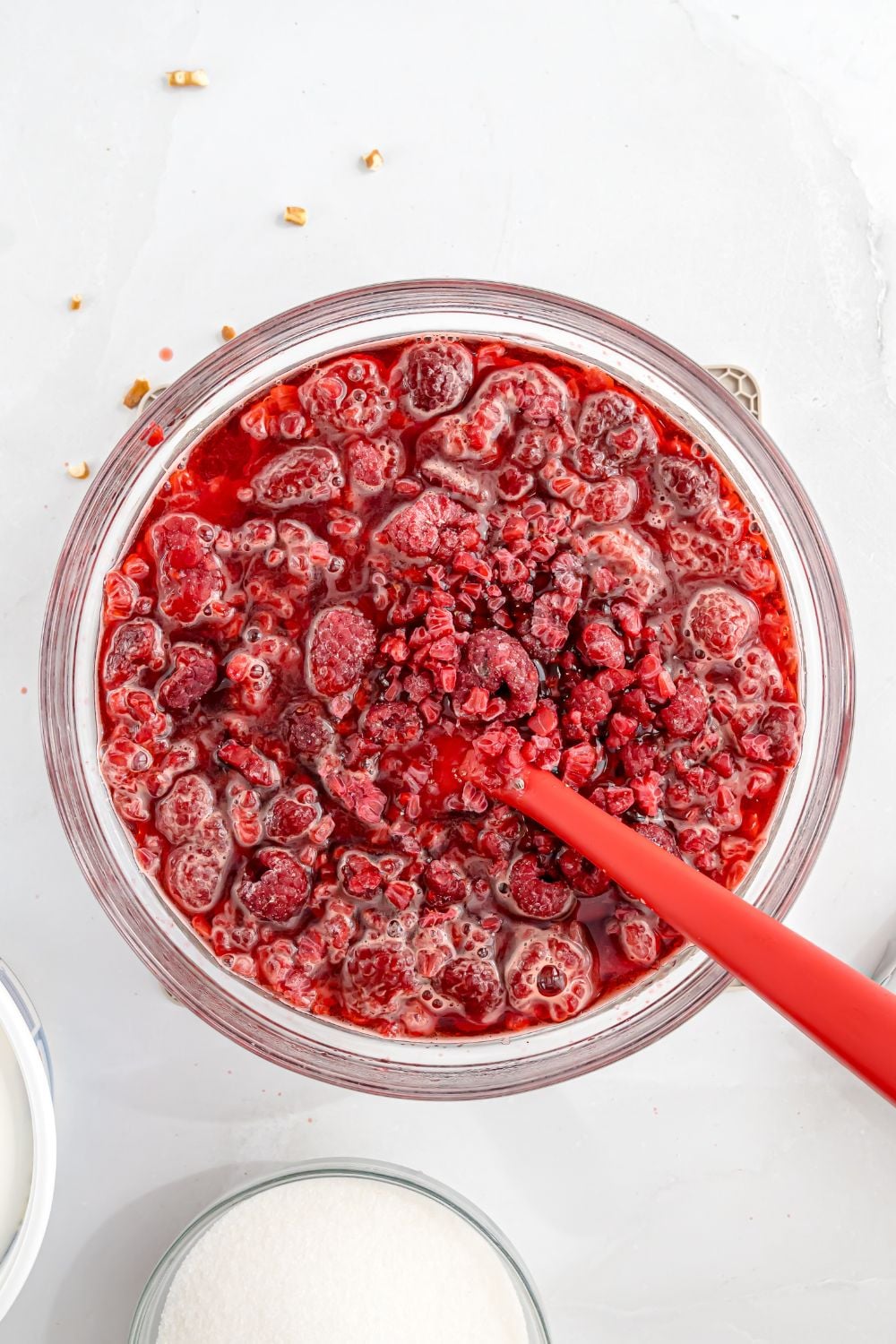 raspberry mixture in a glass bowl being mixed with spatula sitting on the table