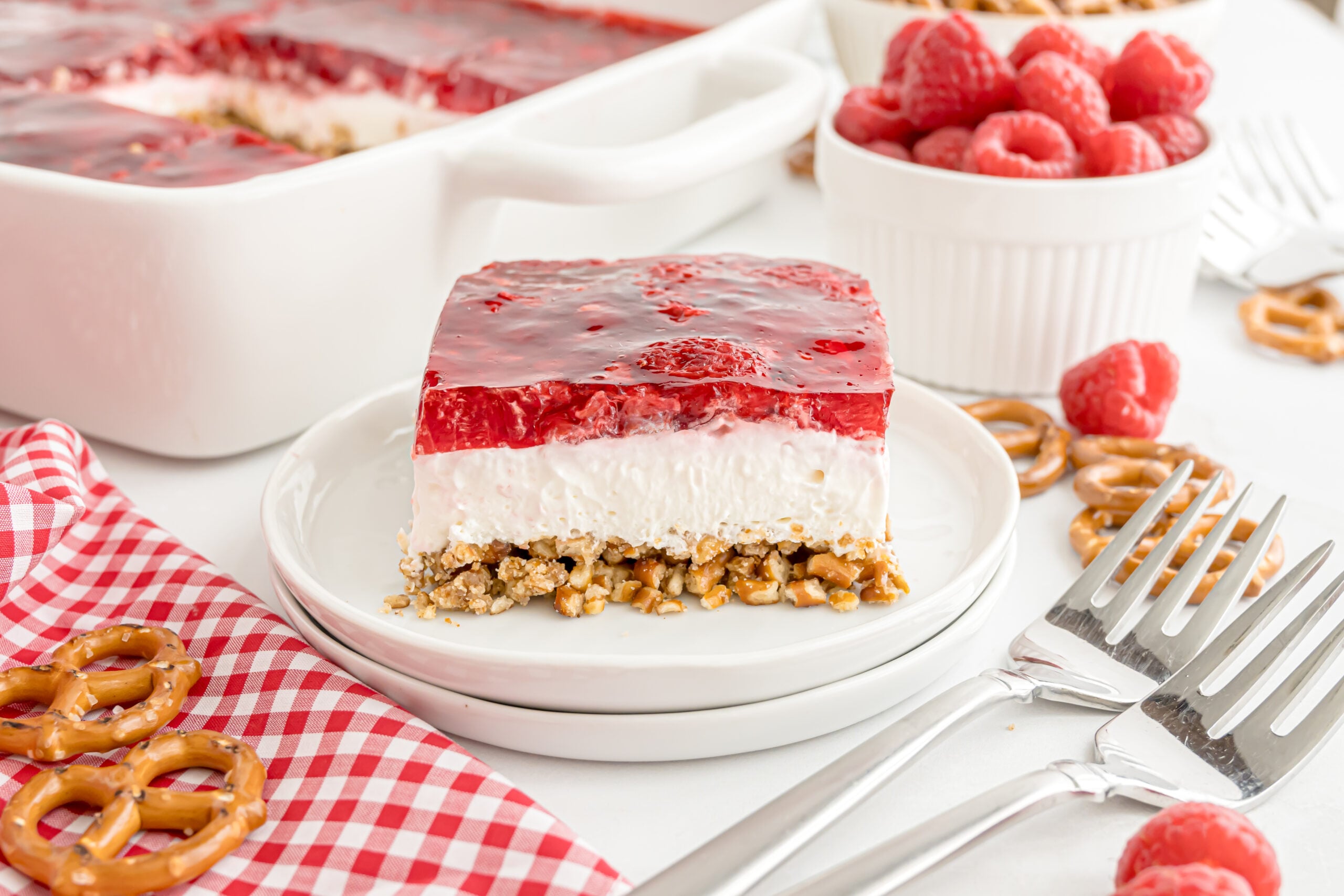 Raspberry Pretzel Salad on a plate with more pretzels and berries scattered around the table