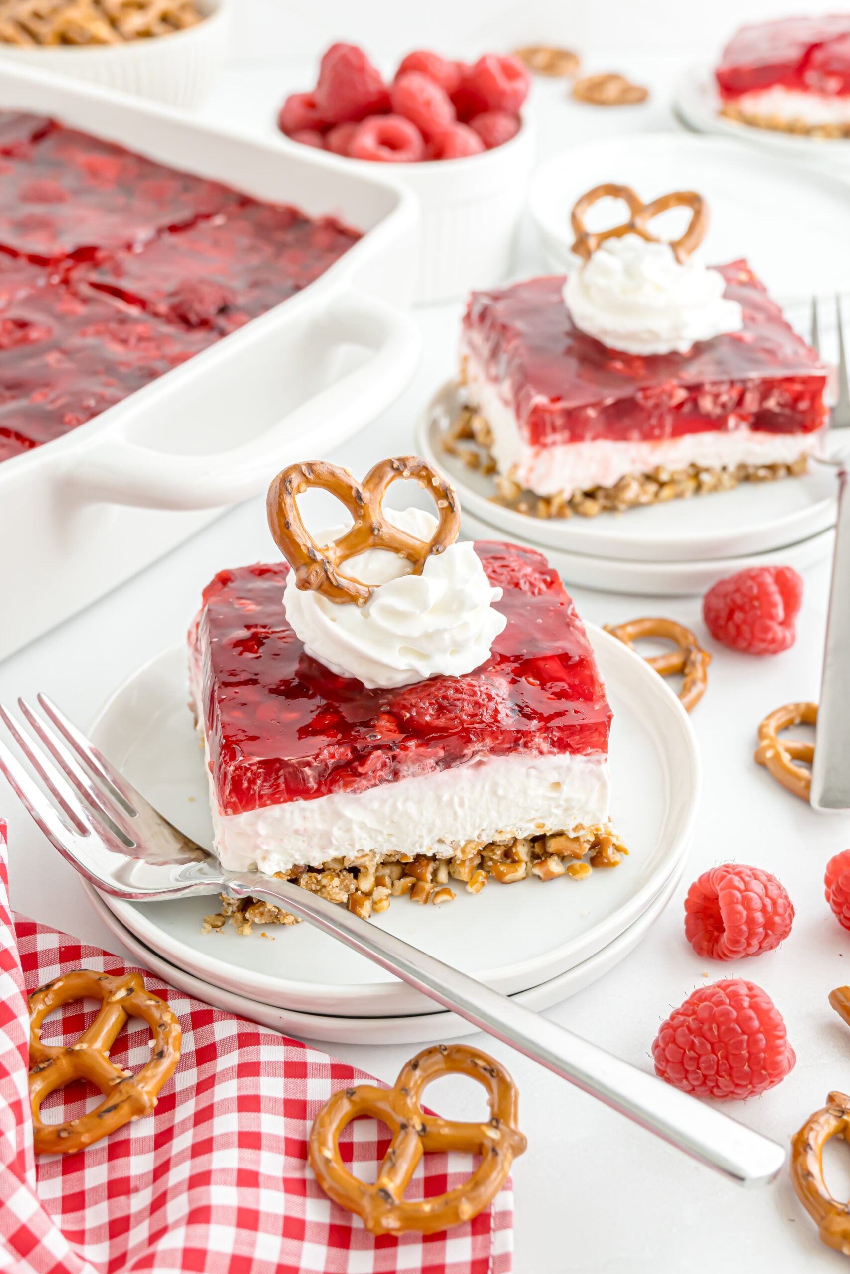 slice of Raspberry Pretzel Salad on a white plate on table with a red checkered napkin to the side