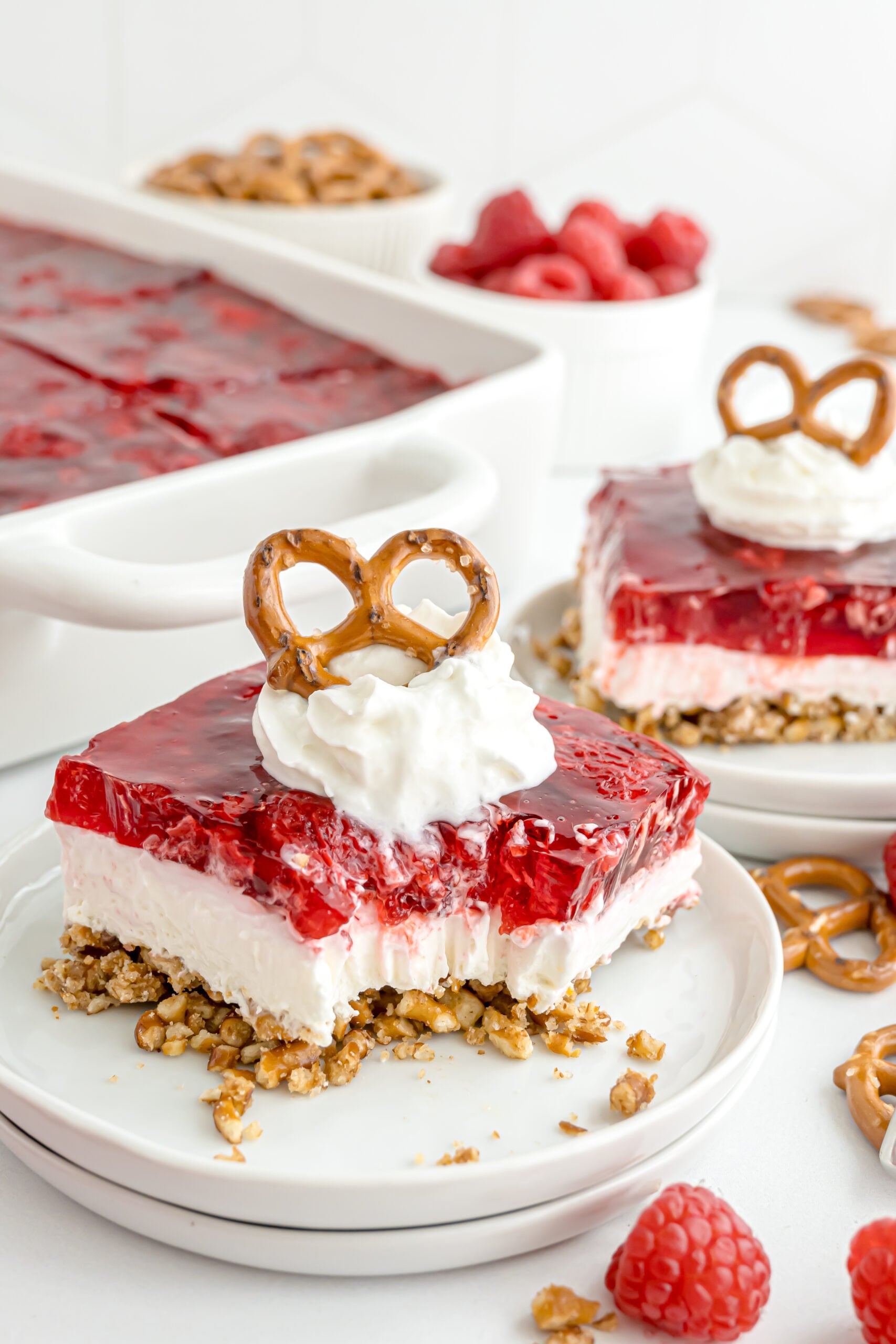 a table with a Raspberry Pretzel Salad on stacked plates with a bite missing