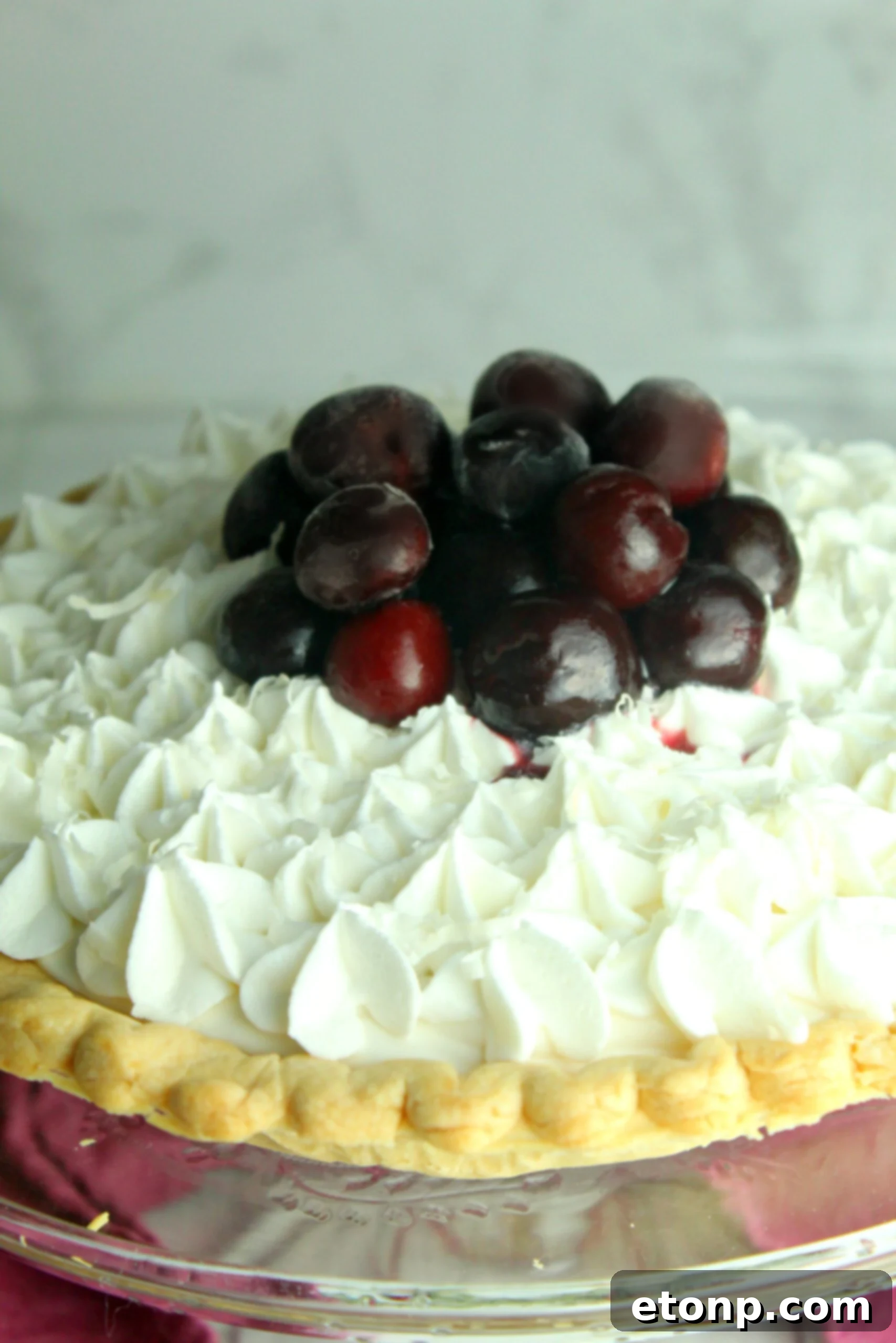 A beautifully crafted White Christmas Pie, perfectly chilled and ready to serve, adorned with bright red cherries and a delicate dusting of coconut. This vintage recipe promises holiday cheer.