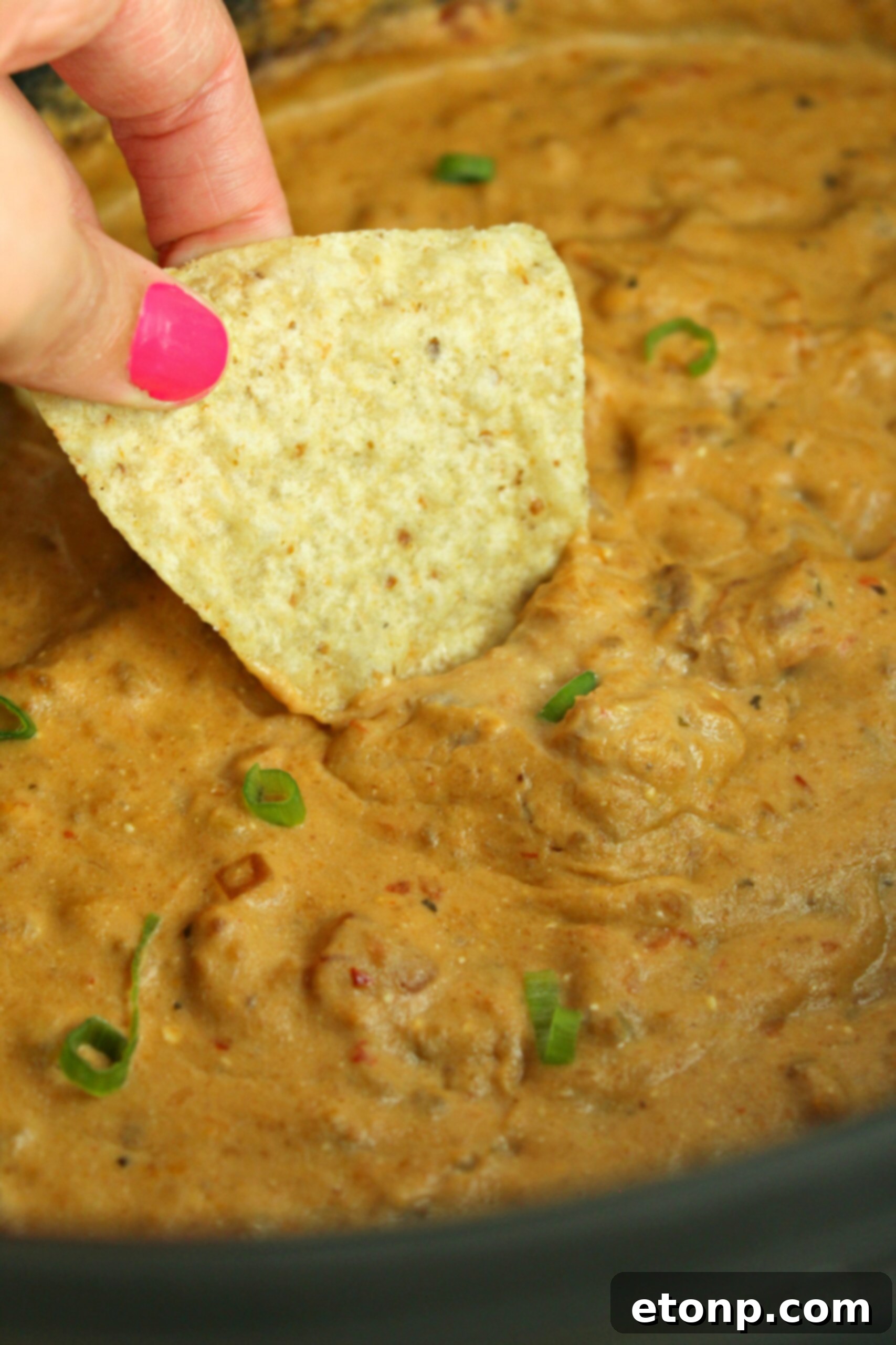 Serving spoonfuls of warm Slow Cooker Taco Dip from the slow cooker onto a plate