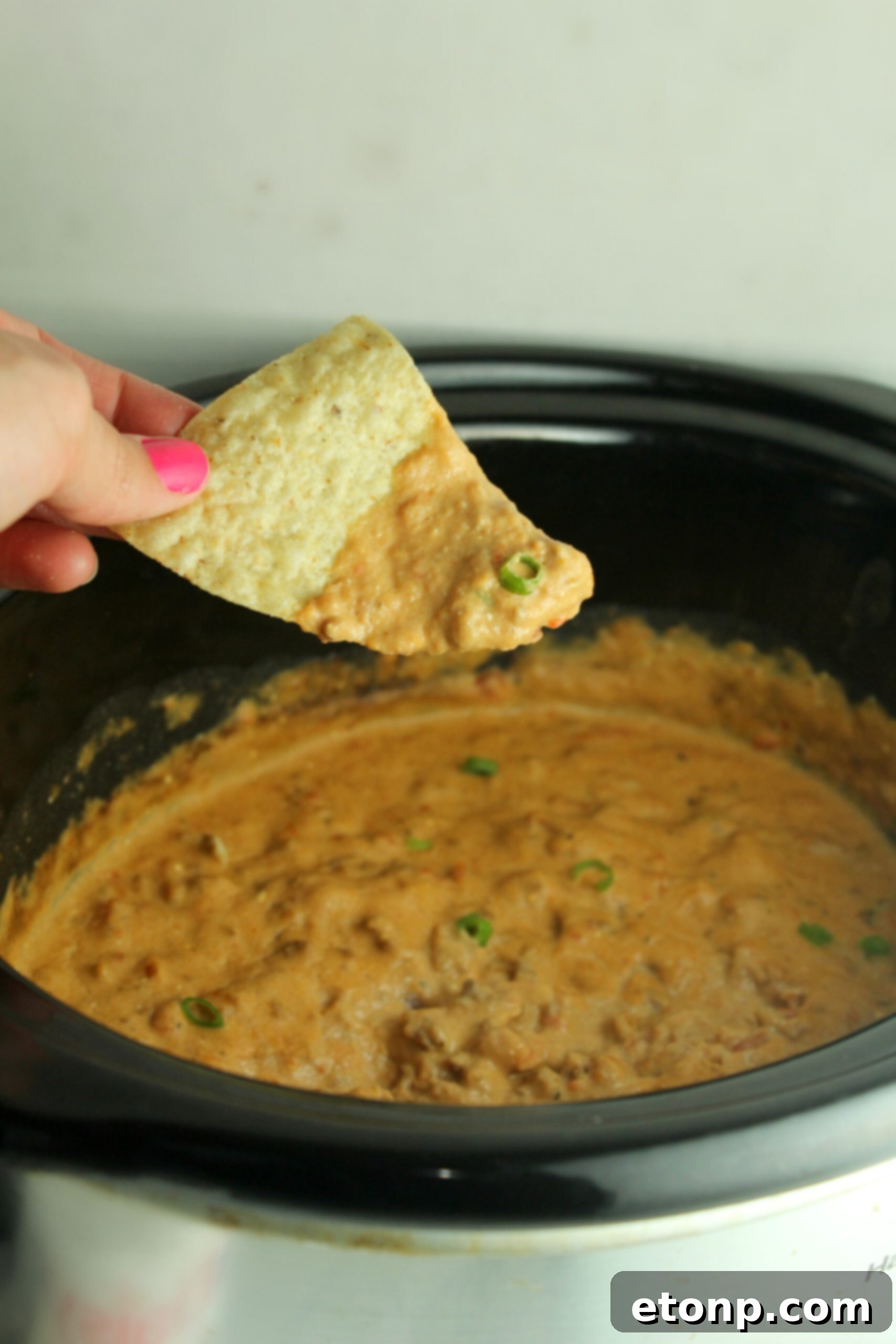 A close-up of a serving of Slow Cooker Taco Dip on a plate with crispy tortilla chips